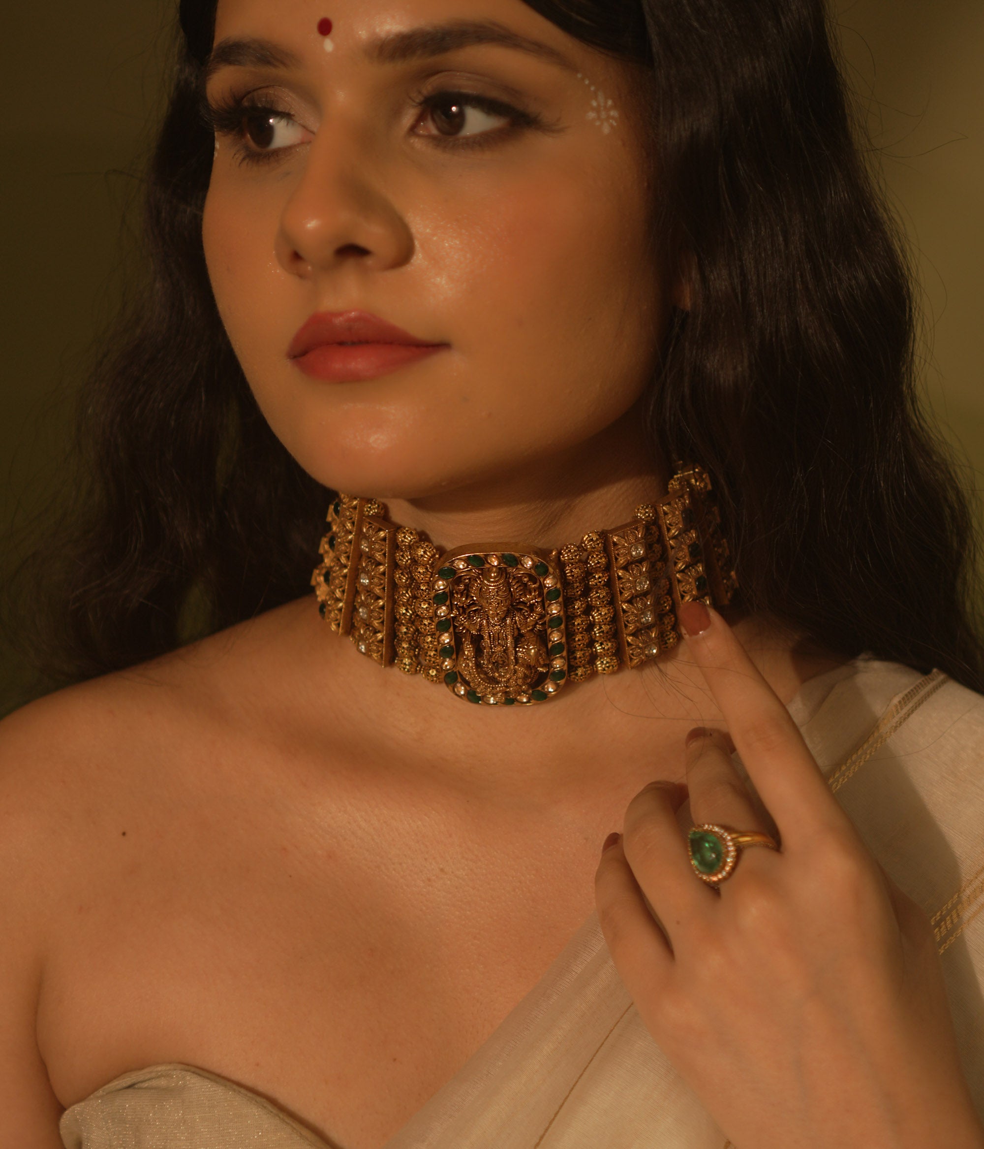 Temple collection Alyaa Necklace featuring Goddess Lakshmi, floral carvings, and emerald green Kundan stones in a choker design.