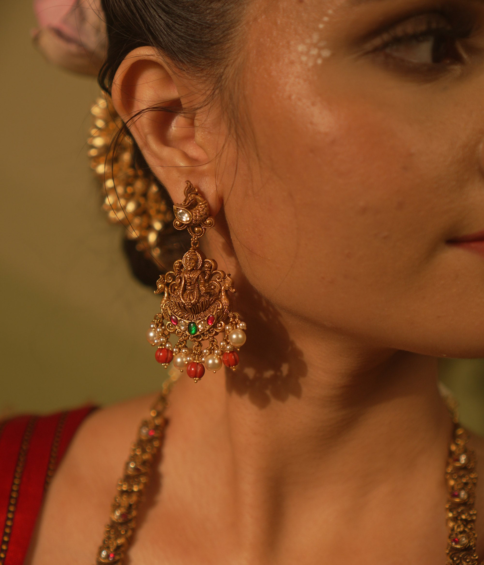 Temple-style Ganesha earrings with red and green Kundan stones, coral beads, and pearls for traditional wear.