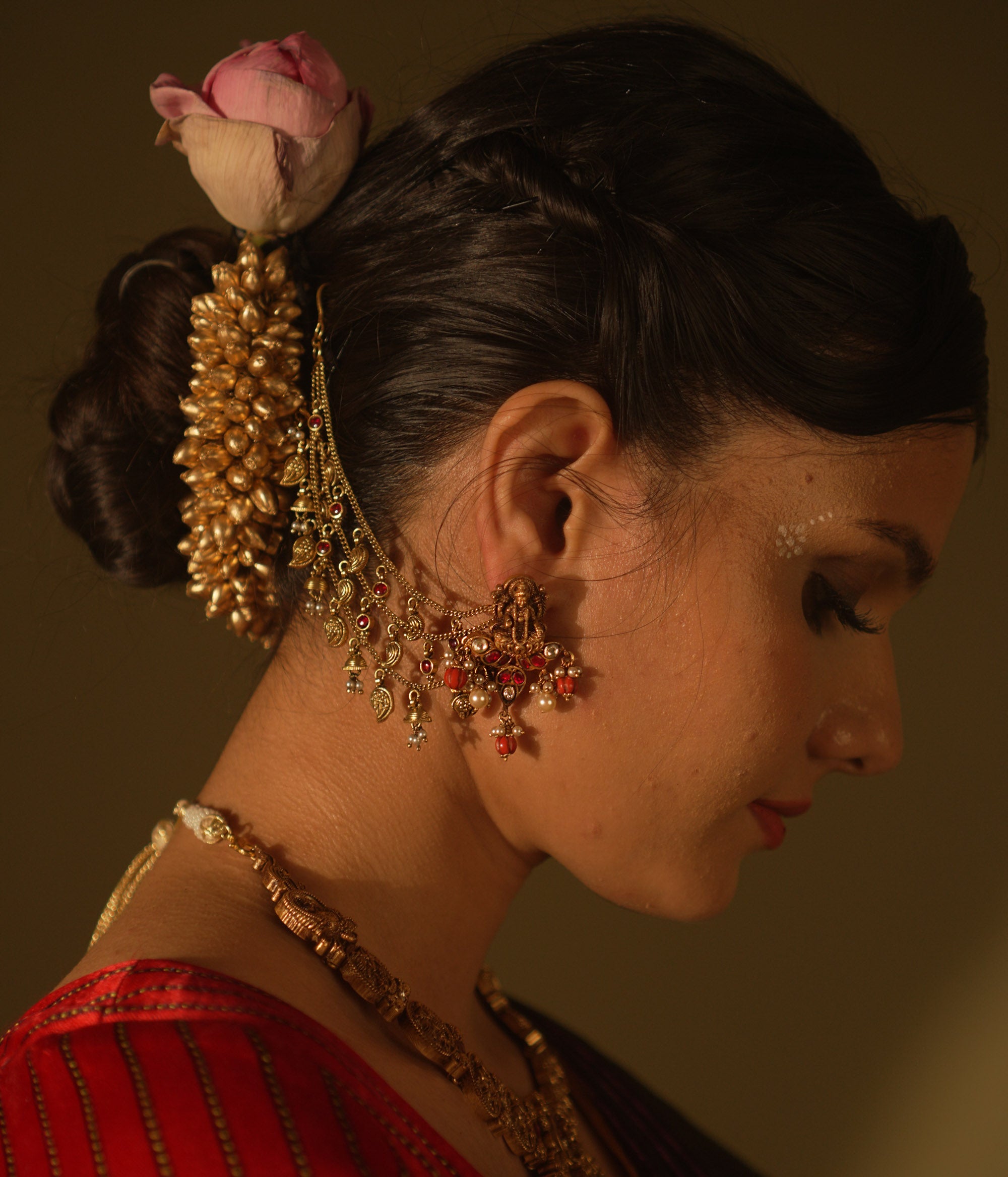 Antique gold temple earrings with a goddess figure, red and green kundan, red beads, and pearls, with multi-strand chains extending to the hair.