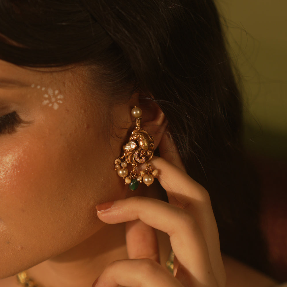 Gold temple earrings with peacock motif, green gemstones, and dangling pearls.