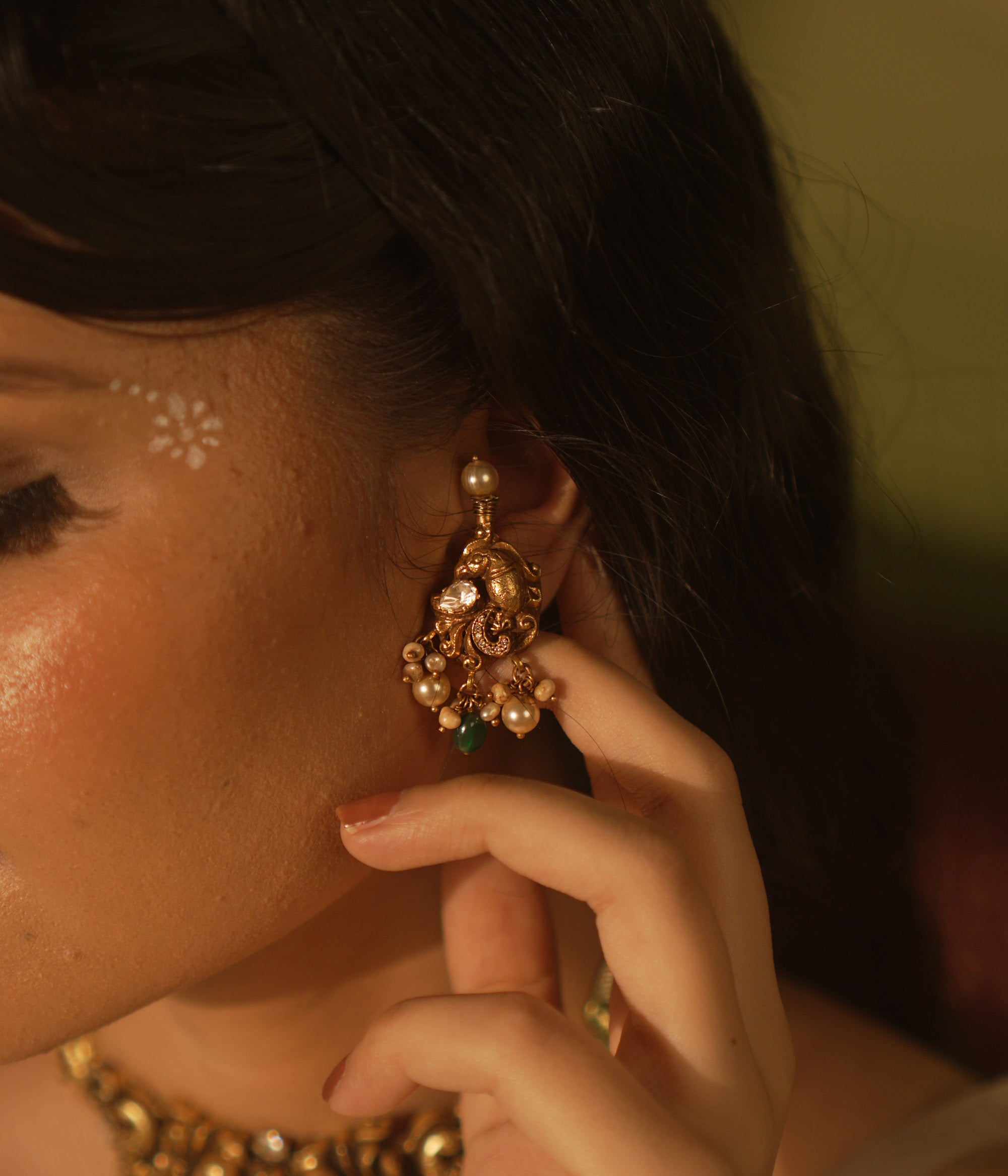 Gold temple earrings with peacock motif, green gemstones, and dangling pearls.
