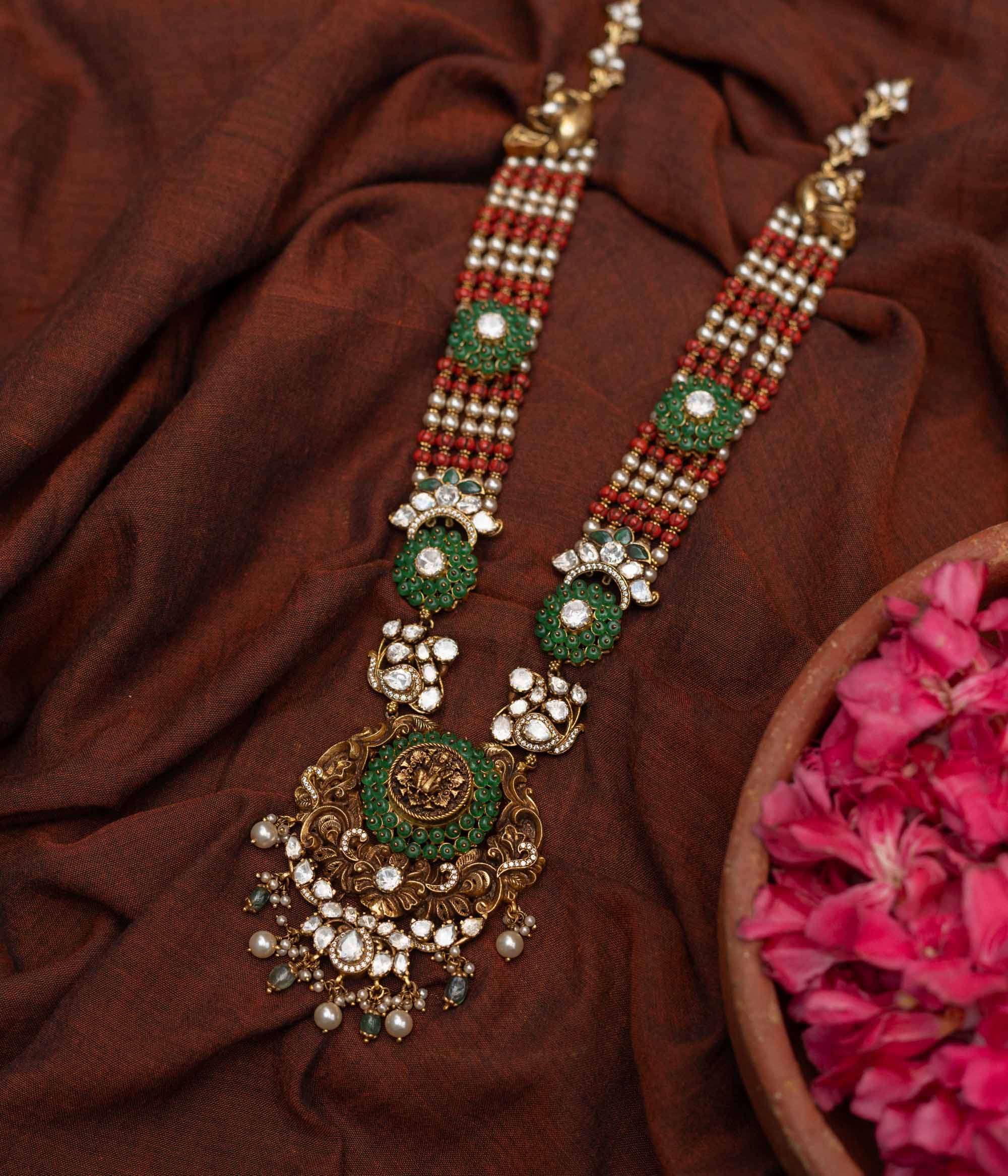 Antique gold-embossed 92.5 sterling silver Devi Lakshmi Necklace inspired by temple art, featuring vibrant green and white stones and cascading pearls from the divine central motif, embodying traditional elegance and spiritual grace.