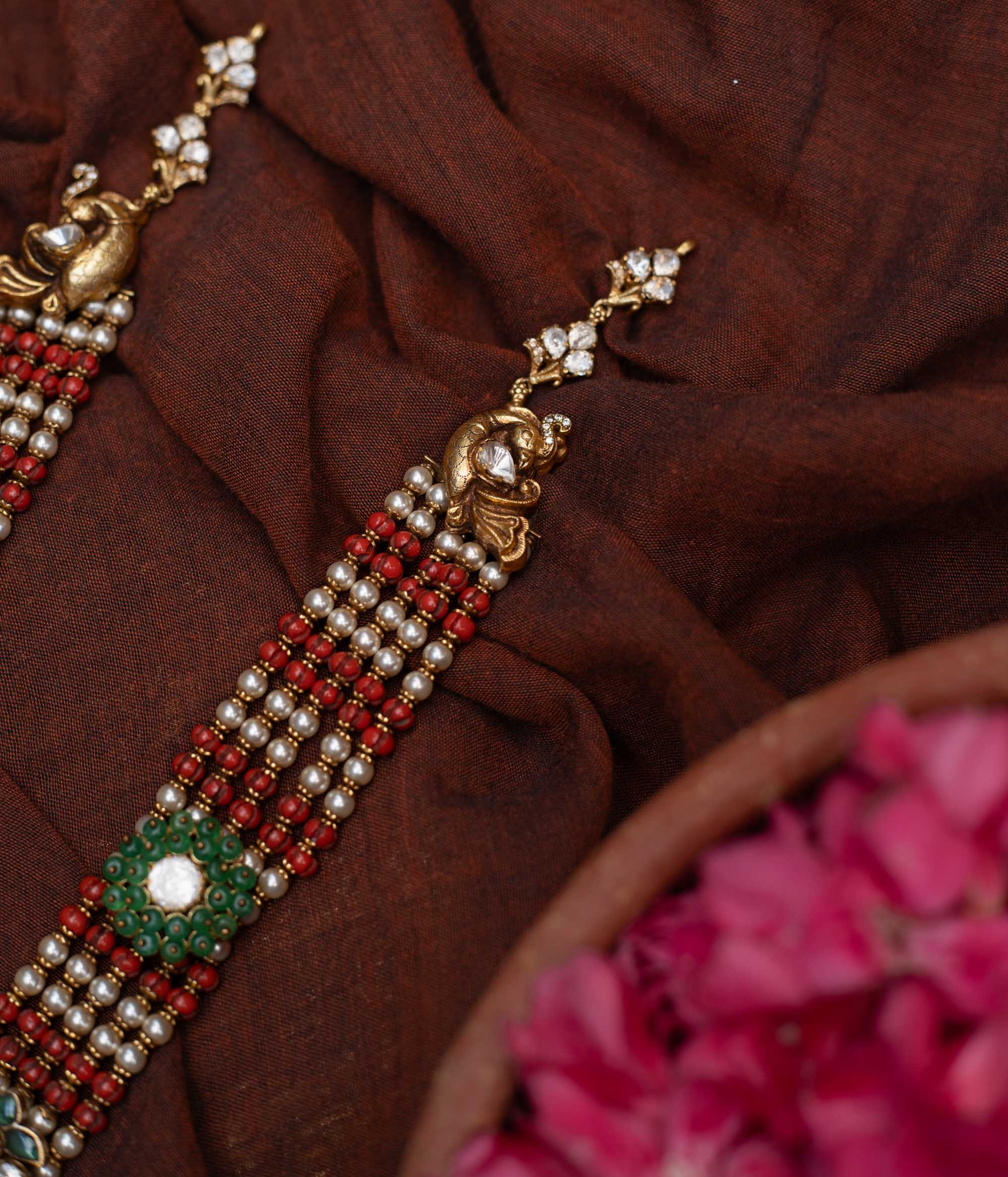 Antique gold-embossed 92.5 sterling silver Devi Lakshmi Necklace inspired by temple art, featuring vibrant green and white stones and cascading pearls from the divine central motif, embodying traditional elegance and spiritual grace.