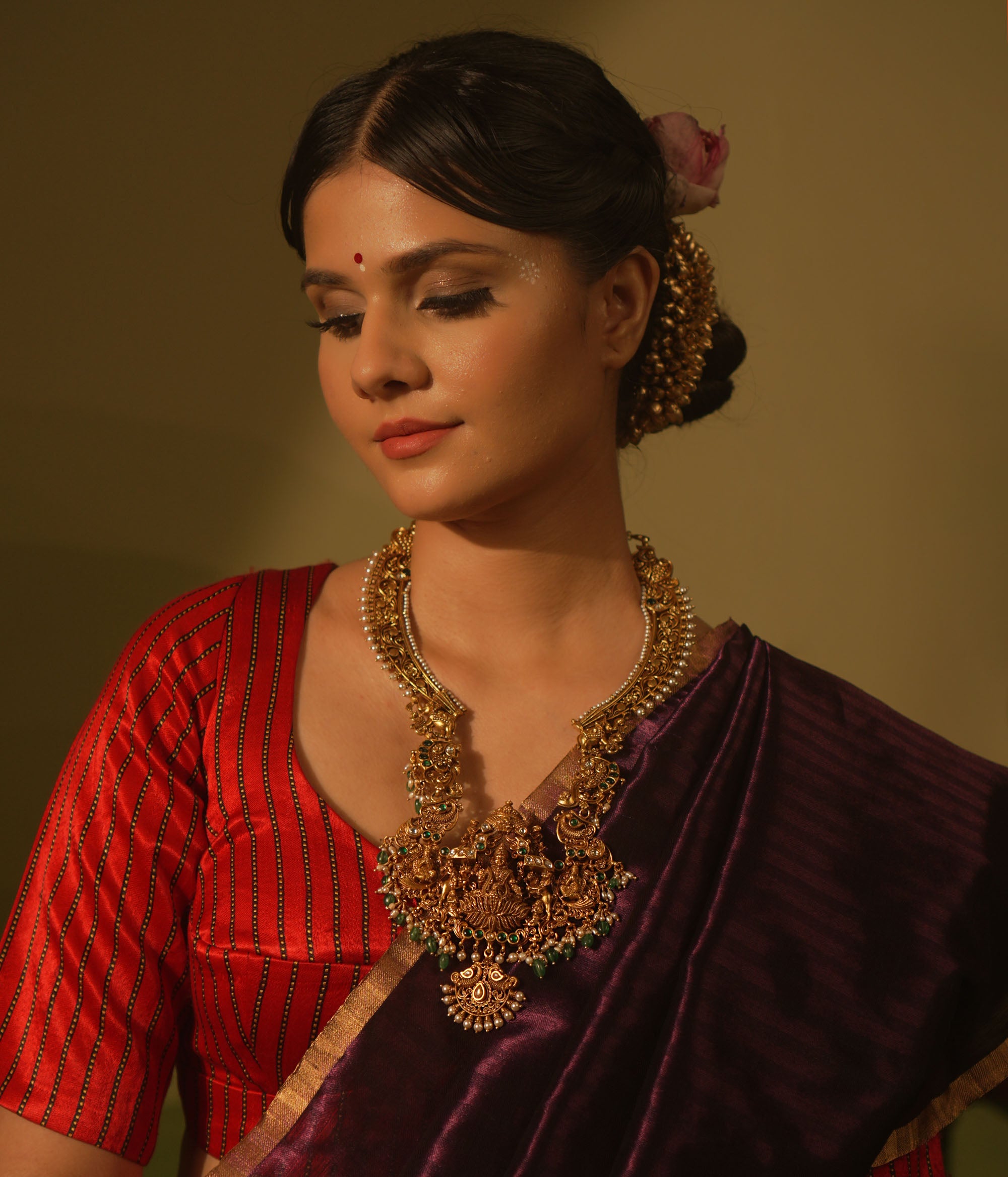 Temple-style gold necklace featuring Goddess Lakshmi, green beads, white Kundan stones, and intricate divine motifs in antique finish.