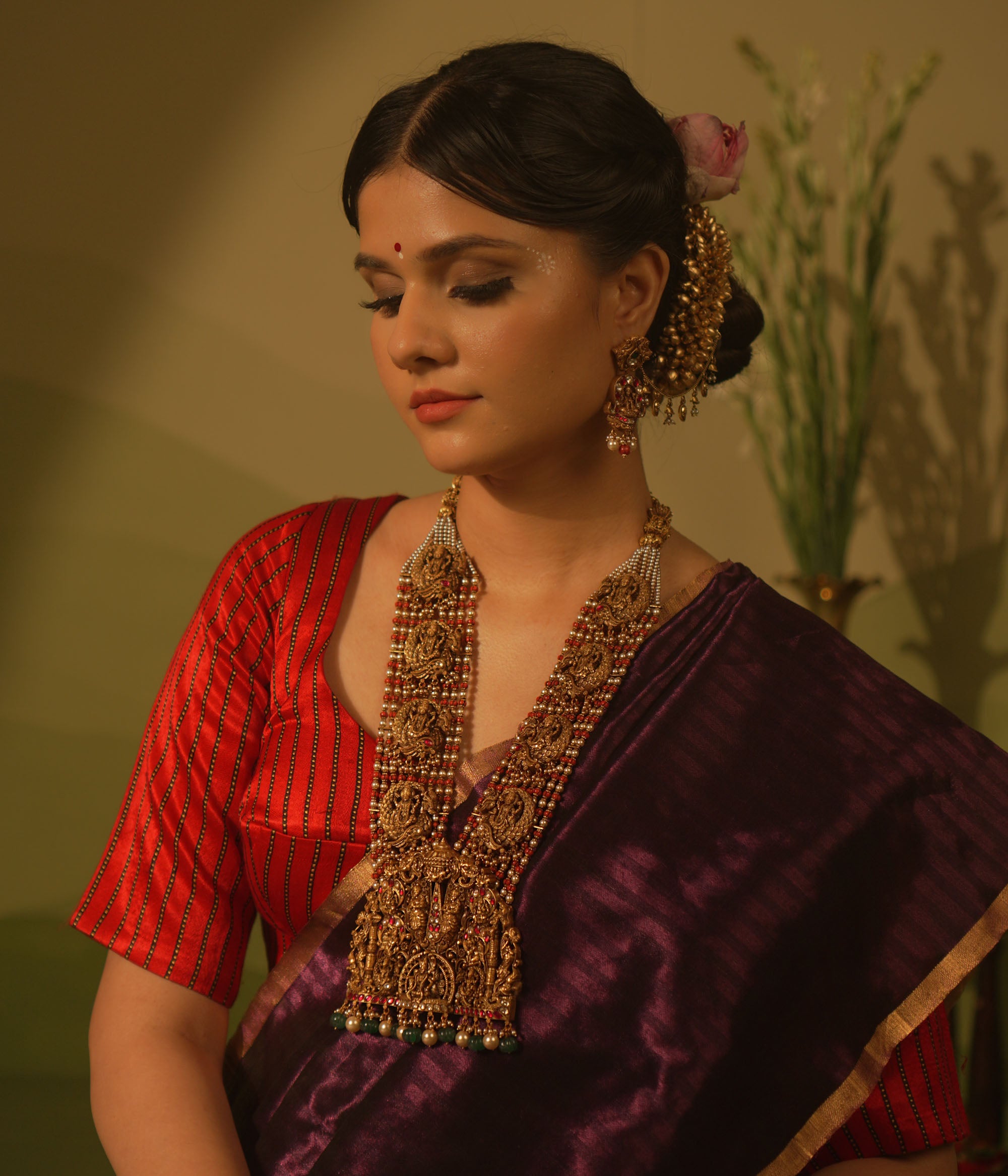 Temple necklace featuring goddess Lakshmi motifs, red and white Kundan stones, green beads, and pearls for traditional bridal wear.