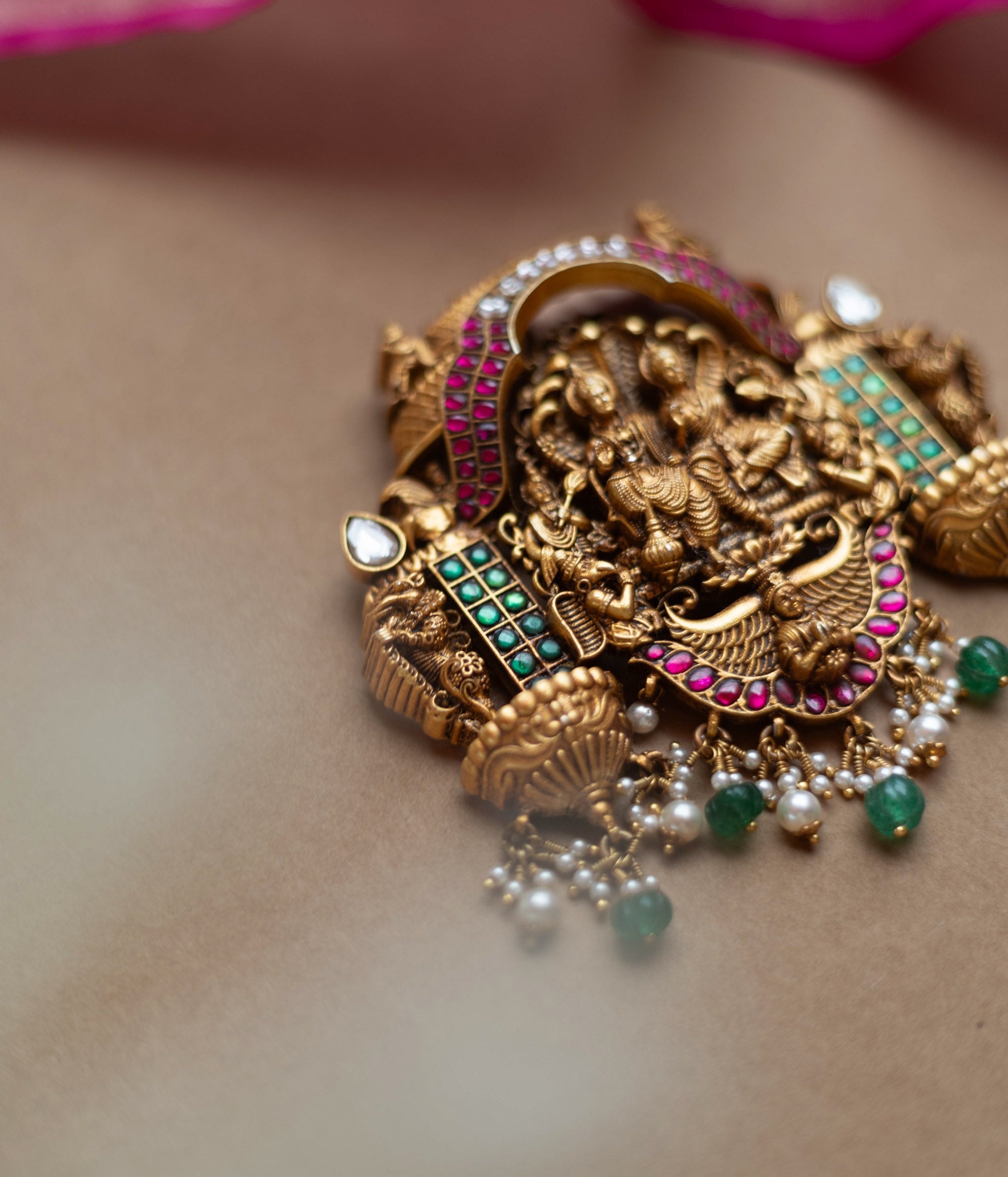 Antique gold temple pendant featuring deities, red, white, and green kundan, green beads, and pearls.