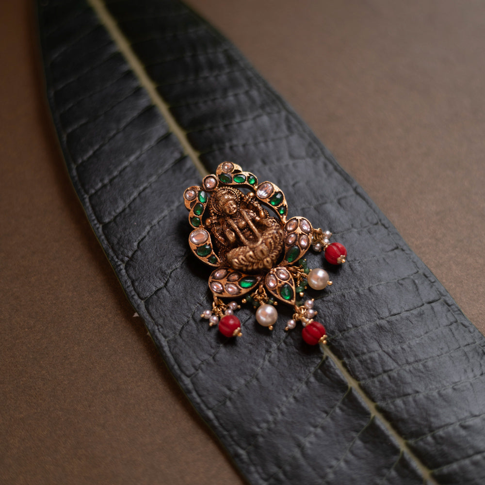 Temple-style pendant featuring Goddess Lakshmi, kundan stones, pearls, and red beads on a green leaf.