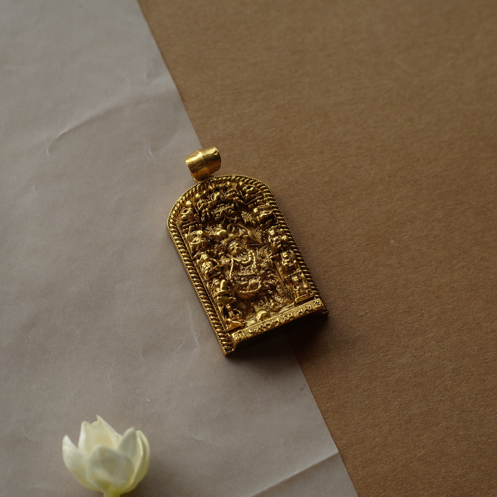 A gold pendant with a crescent-moon and floral design. It features a central red stone surrounded by clear stones and a halo of golden beads, resting on a stone.
