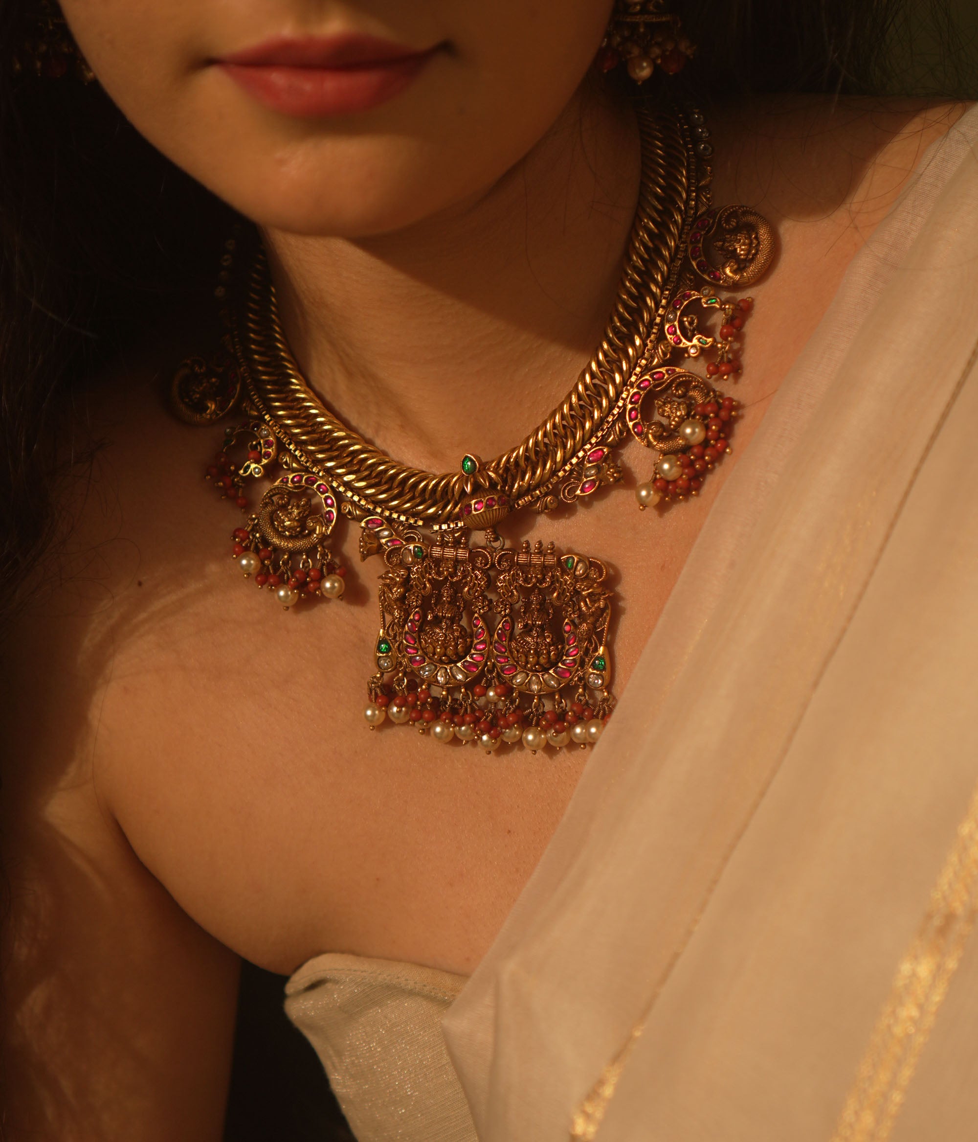 Gold temple necklace with pink kundan peacock pendants, carved deity, pearls, and coral.