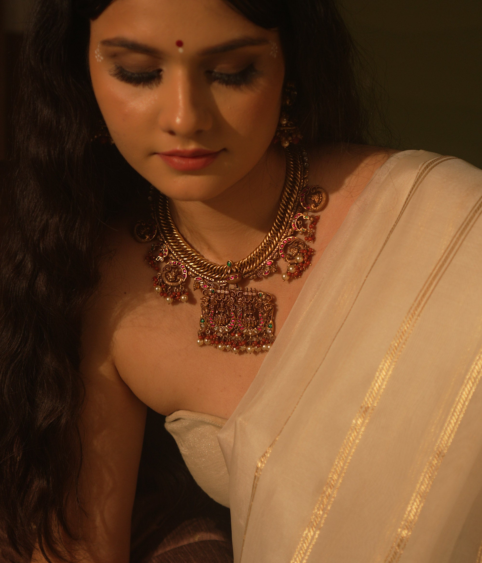 Gold temple necklace with pink kundan peacock pendants, carved deity, pearls, and coral.
