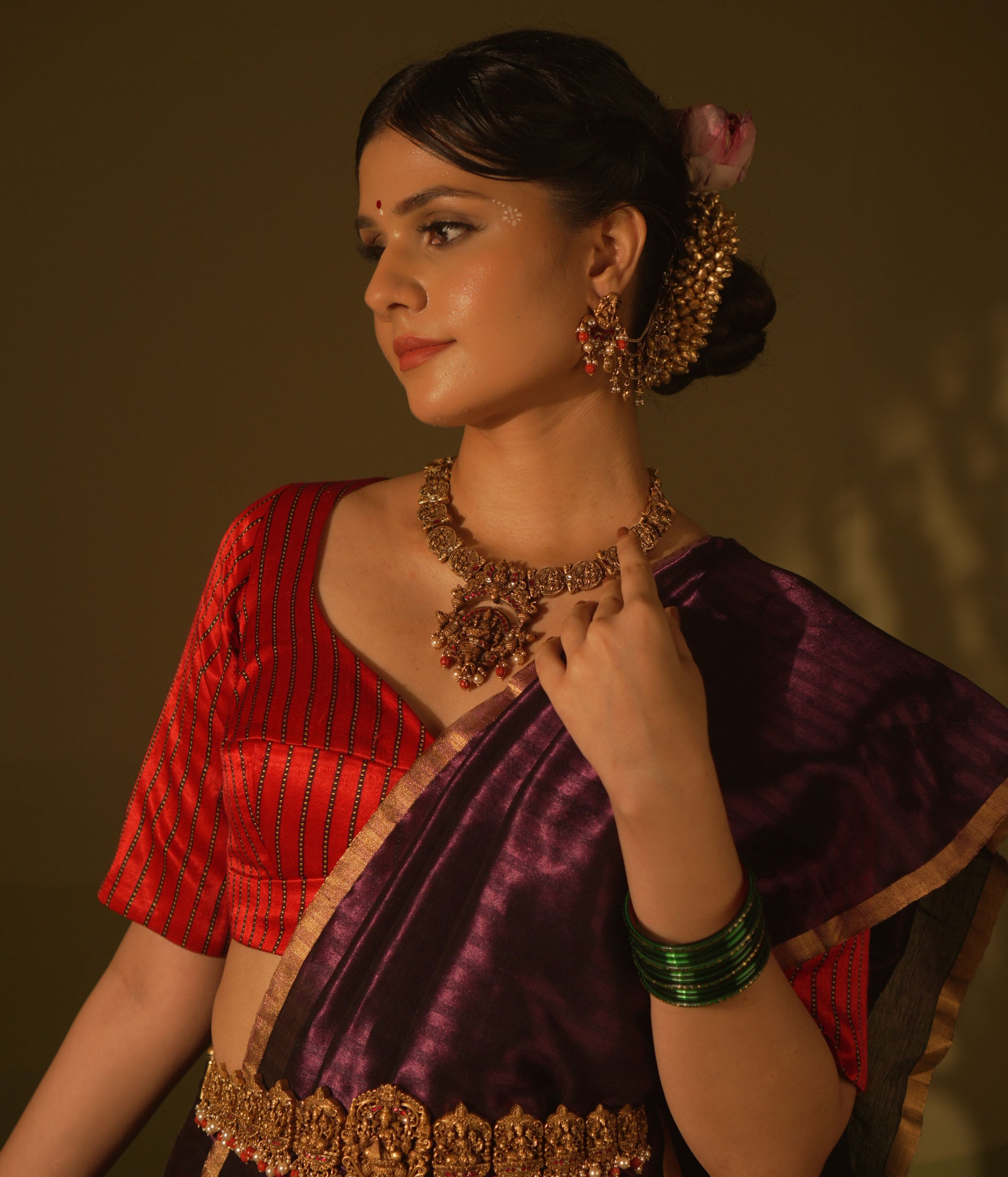 Antique gold temple necklace with goddess motifs, red and white kundan, red beads, and pearl drops, worn by a woman.