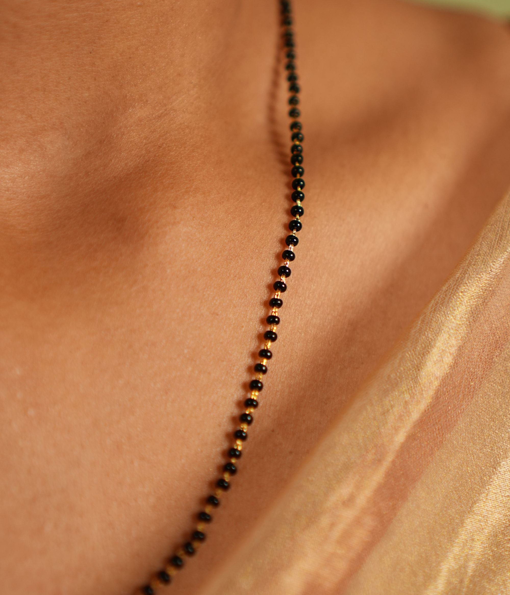woman wearing a delicate black-beaded Mangal Sutra chain with subtle gold accents, resting gracefully on her neckline, paired with a muted saree in earthy tones."