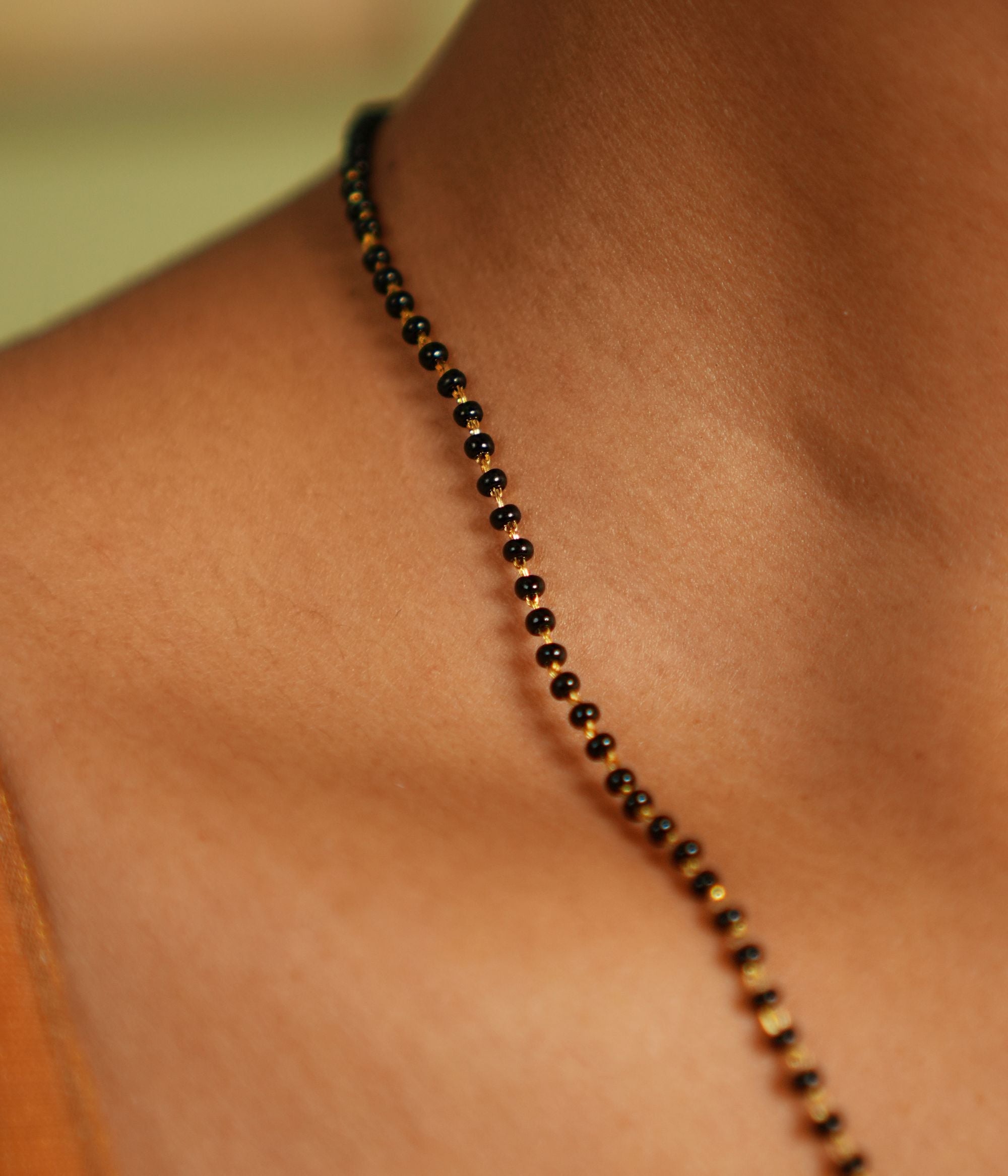 woman wearing a delicate black-beaded Mangal Sutra chain with subtle gold accents, resting gracefully on her neckline, paired with a muted saree in earthy tones."