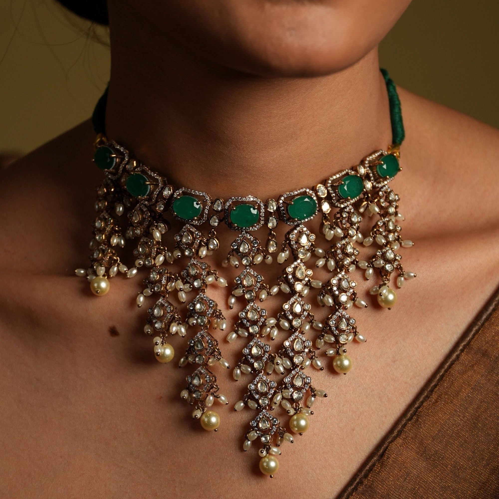 Close-up of a person wearing an ornate necklace with green stones and pearl-like beads.
