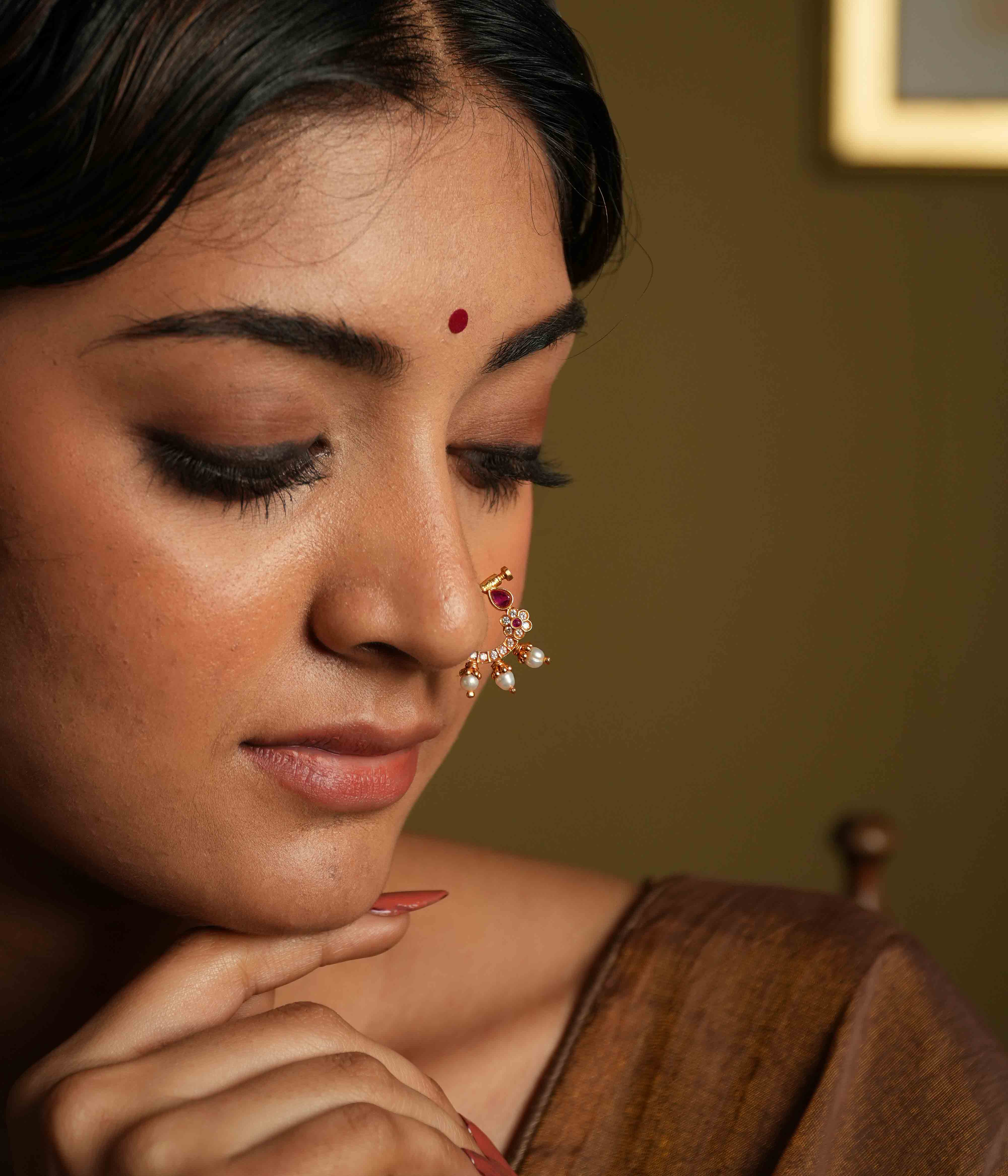 A gold-plated 92.5 sterling silver nose ring featuring a vintage South Indian-inspired design. It is adorned with CZ stones and red cut stones, set in a white Kundan setting. The piece includes a minimal flower motif with three bold pearl edgings, exuding timeless elegance and classic sophistication.