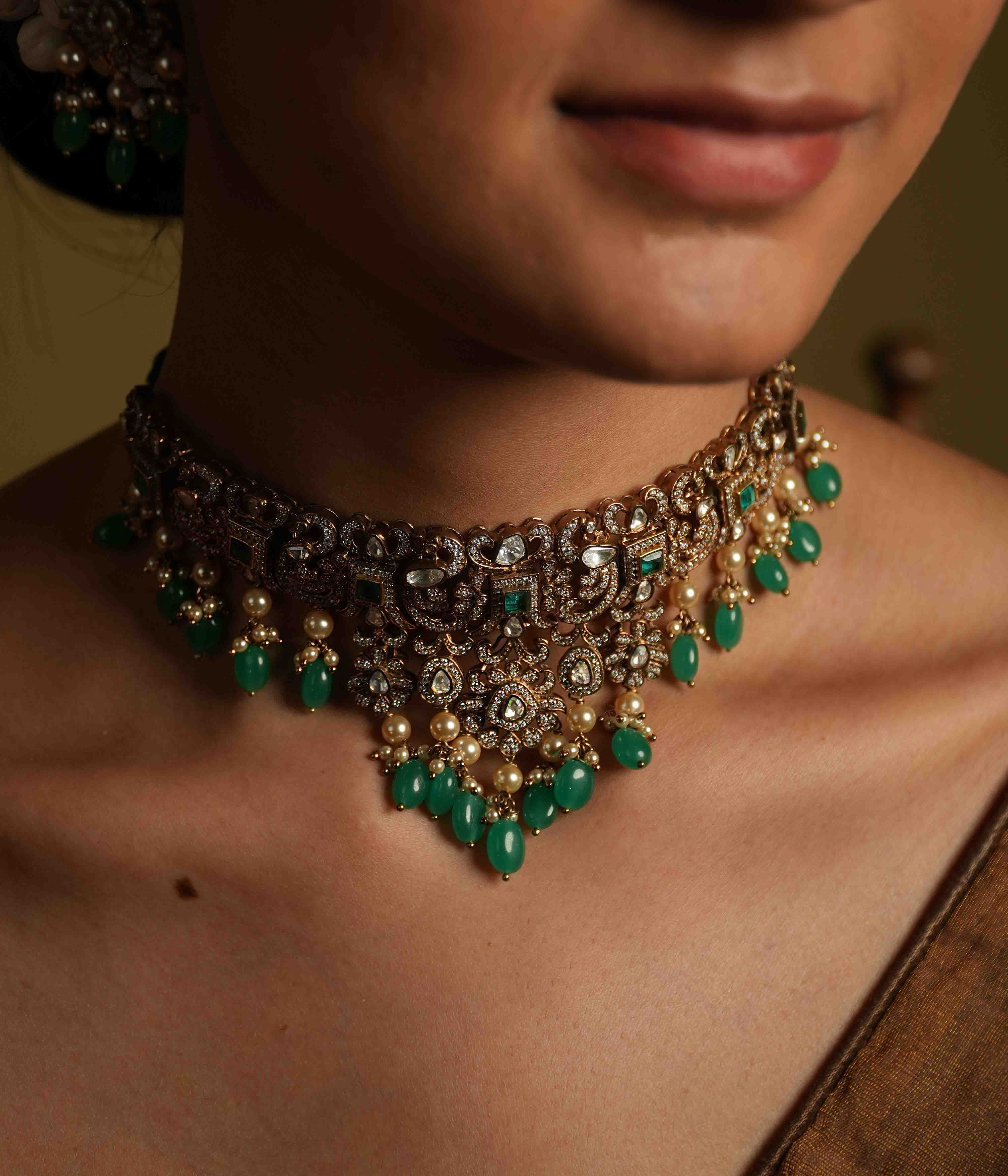 A handcrafted 92.5 sterling silver and 14ct dark antique gold plated choker, featuring moissanite, CZ stones, polki stones, and green spinel stones, finished in a Victorian style, with delicate pearl dangles, evoking regal romance and the opulence of a bygone era.
