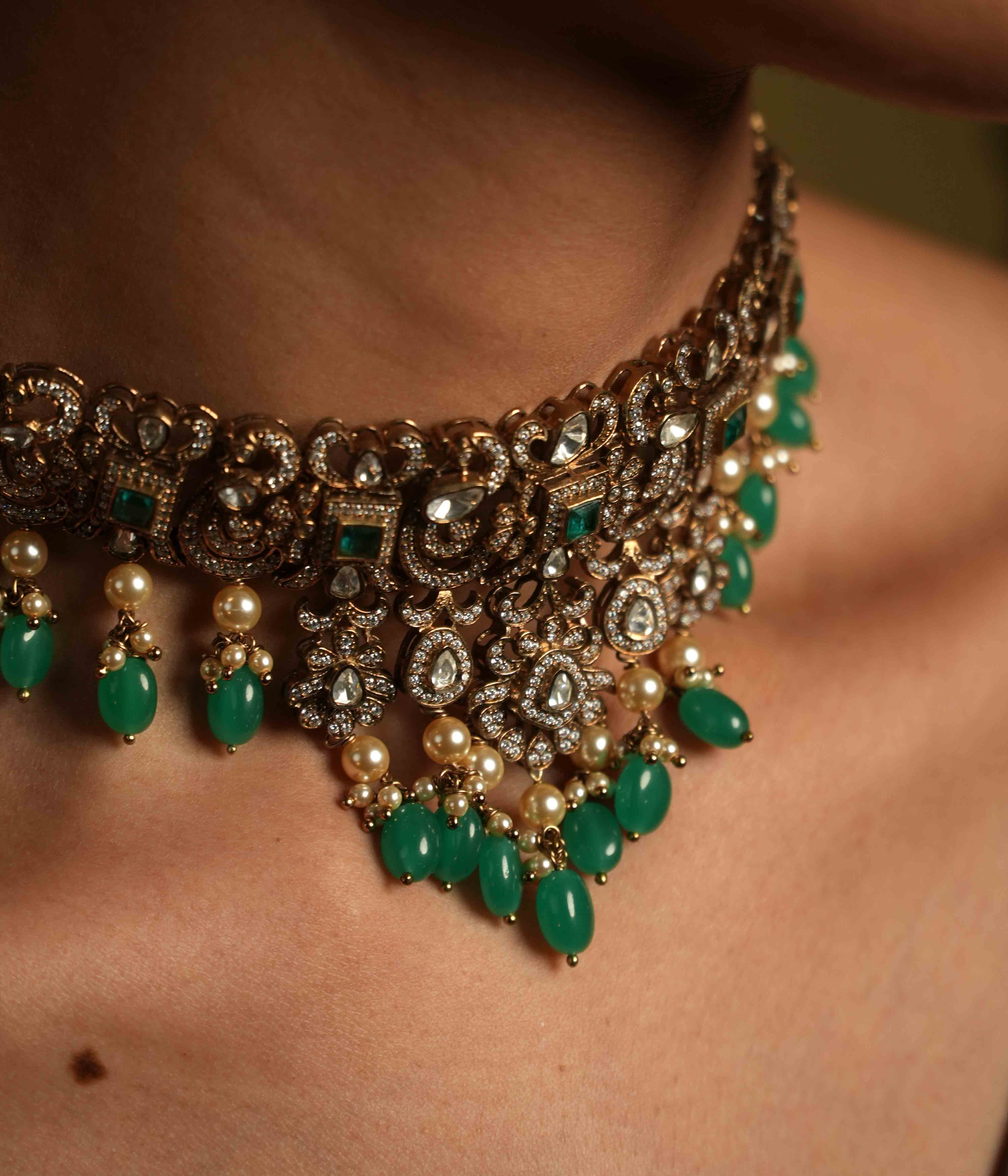 A handcrafted 92.5 sterling silver and 14ct dark antique gold plated choker, featuring moissanite, CZ stones, polki stones, and green spinel stones, finished in a Victorian style, with delicate pearl dangles, evoking regal romance and the opulence of a bygone era.