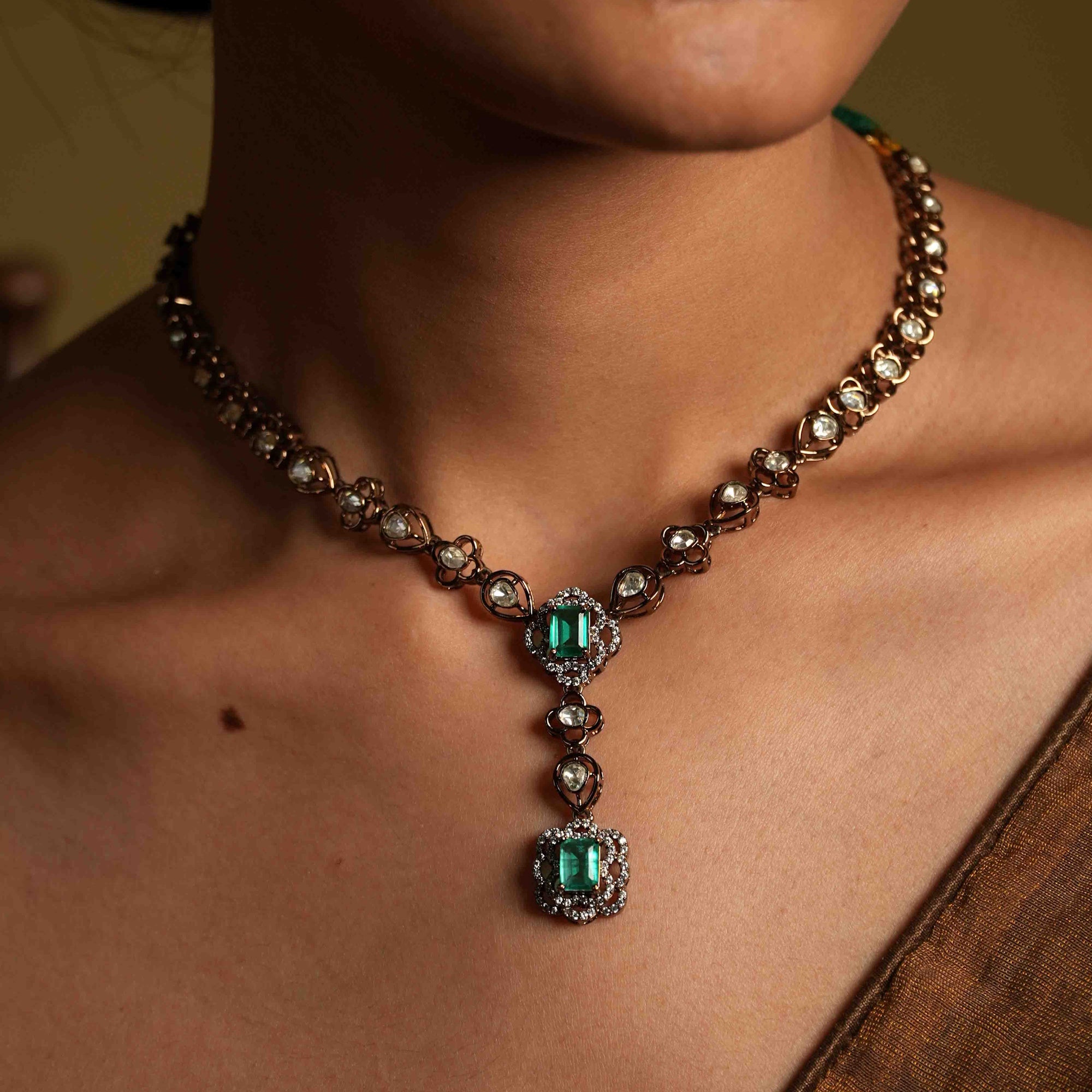 Close-up of a person wearing an ornate necklace with emerald green gemstones.