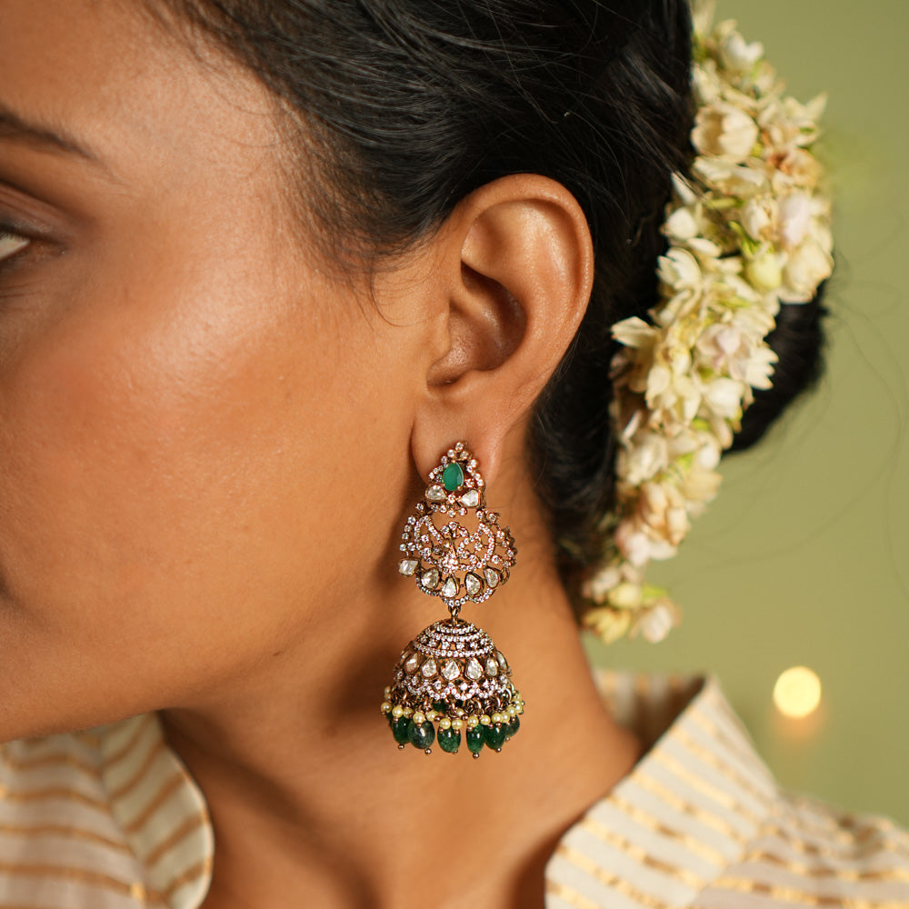Exquisite gold-plated silver jhumkas featuring a graceful floral design, adorned with vibrant green gemstones, sparkling Polki stones, shimmering CZ stones, delicate pearls, and elegant green beads, offering a perfect blend of tradition and sophistication.