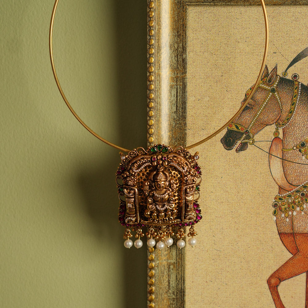 Traditional gold-plated silver temple jewelry pendant featuring Goddess Lakshmi at the center, adorned with radiant red and green Kundan stones and elegant pearl drops. Designed with both single and double hooks for versatile styling, this pendant exudes divine grace and timeless craftsmanship.