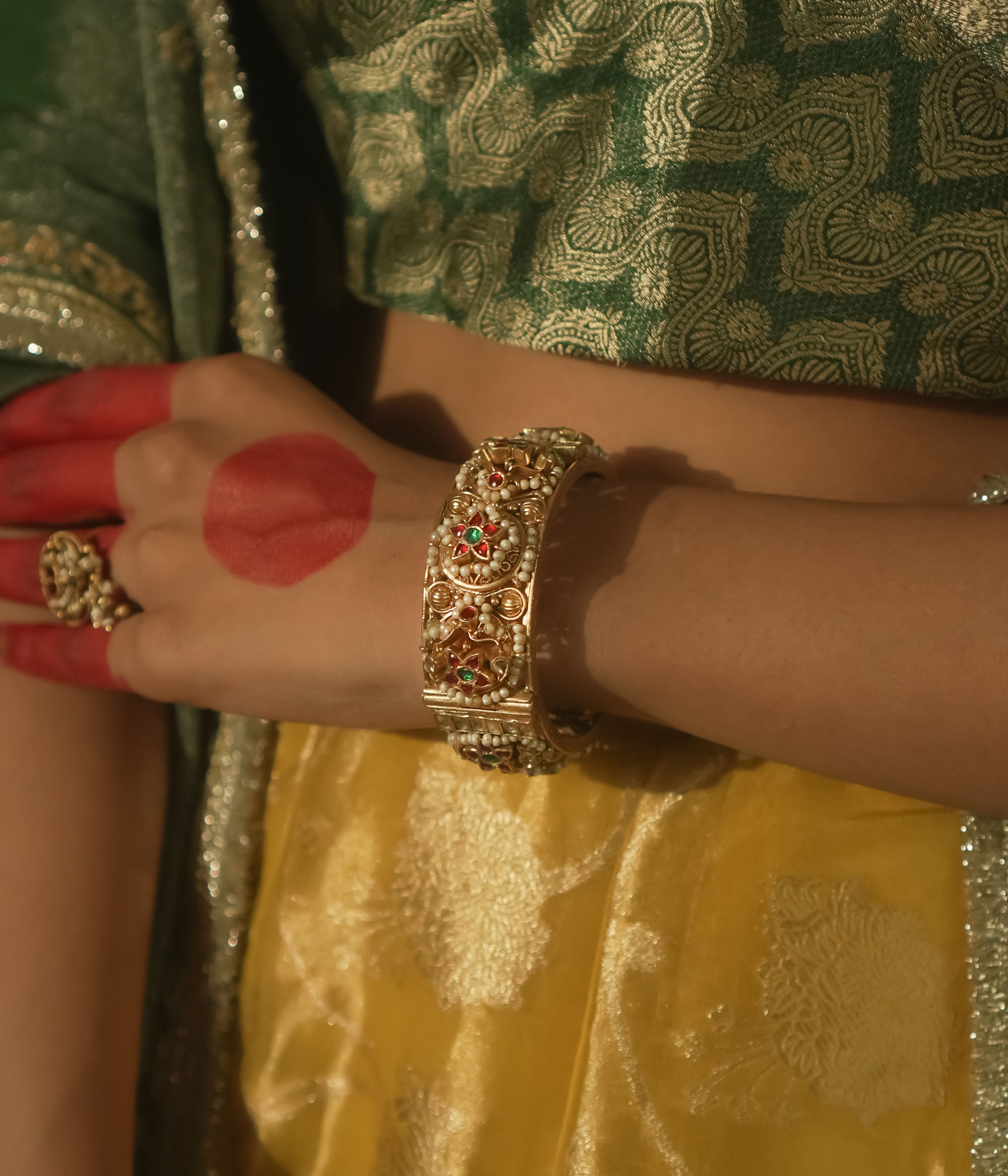 Gold-plated bangle with red and green Kundan gems and intricate patterns.