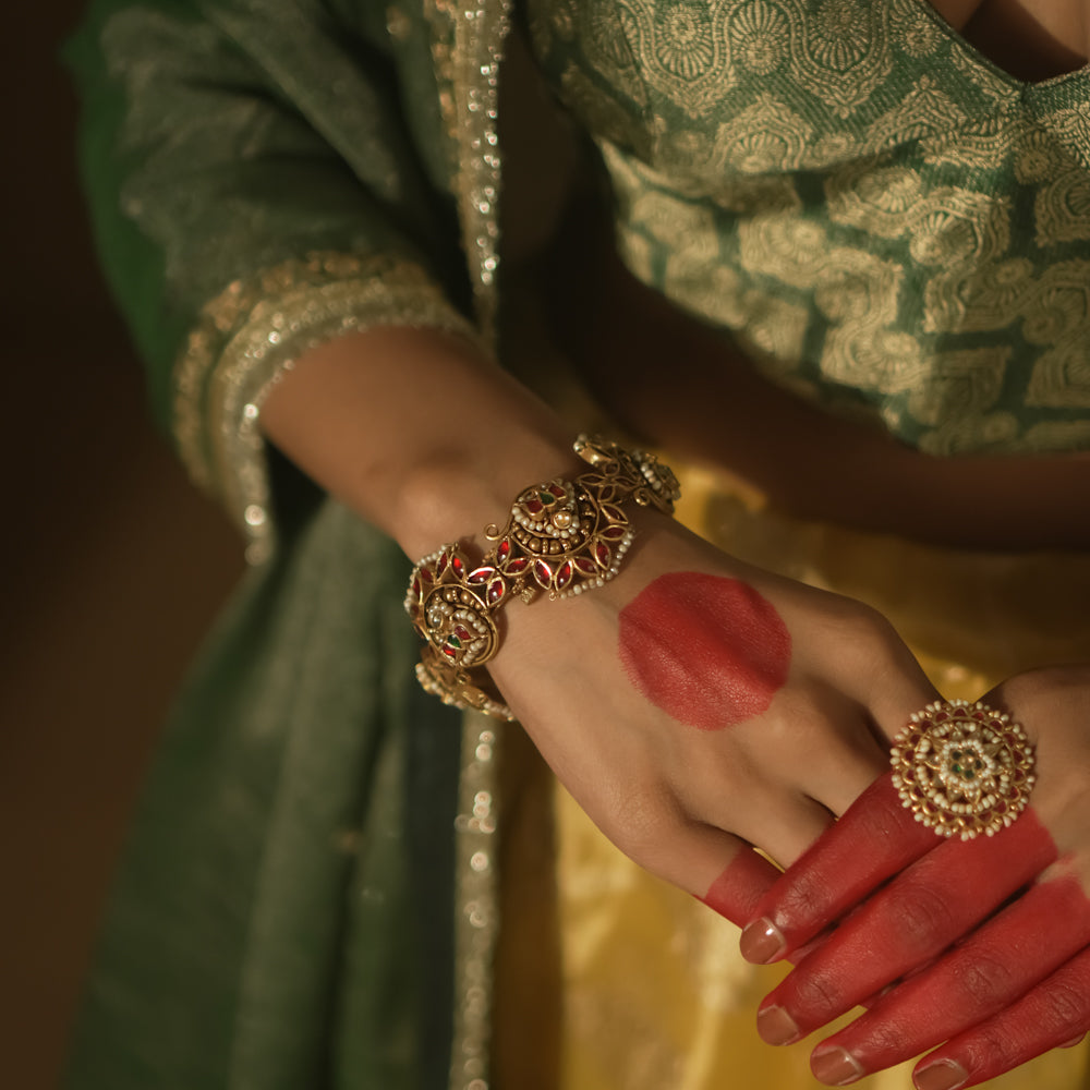 Gold-plated silver bangle with filigree, red Kundan gems, and pearls.