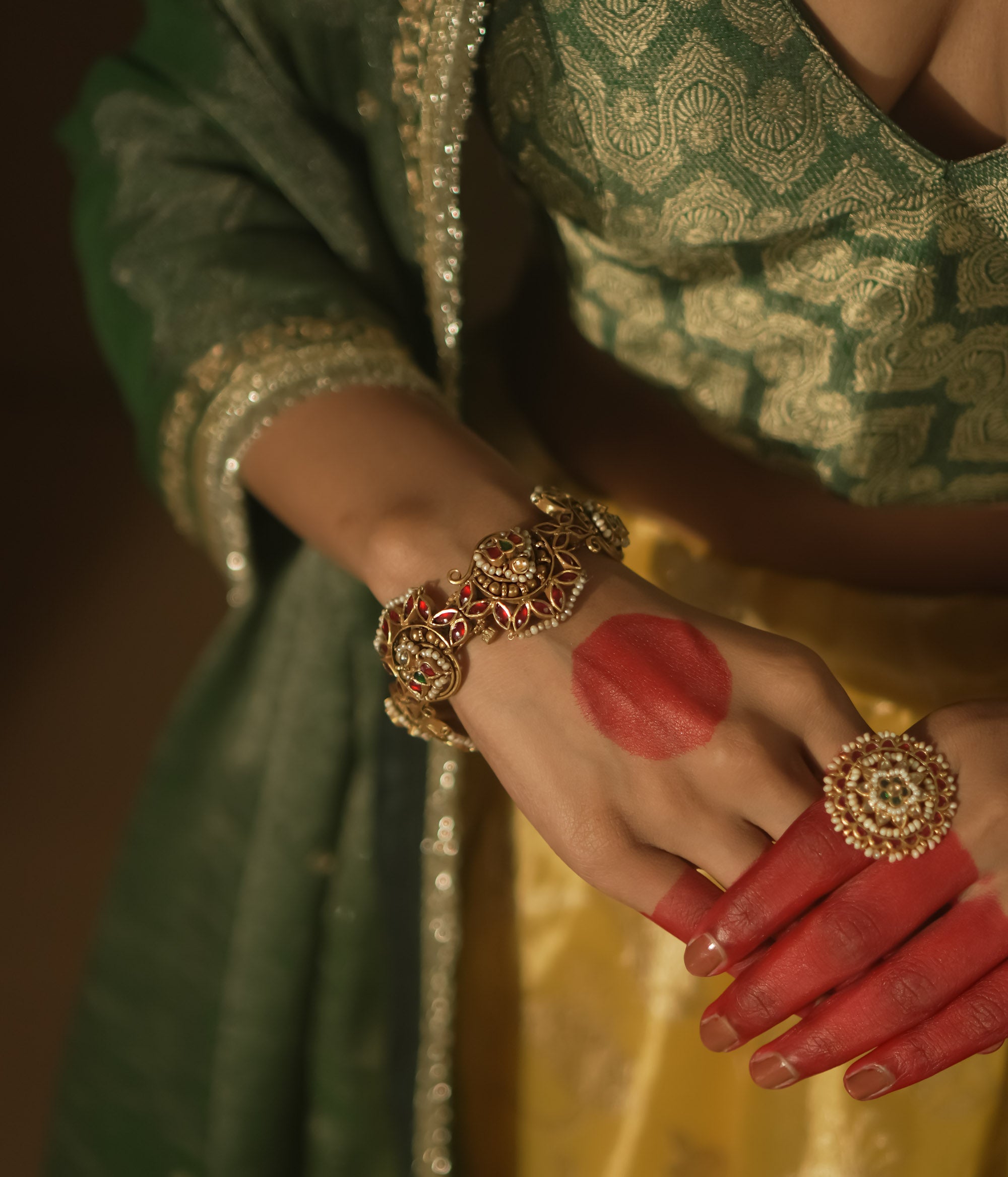 Gold-plated silver bangle with filigree, red Kundan gems, and pearls.