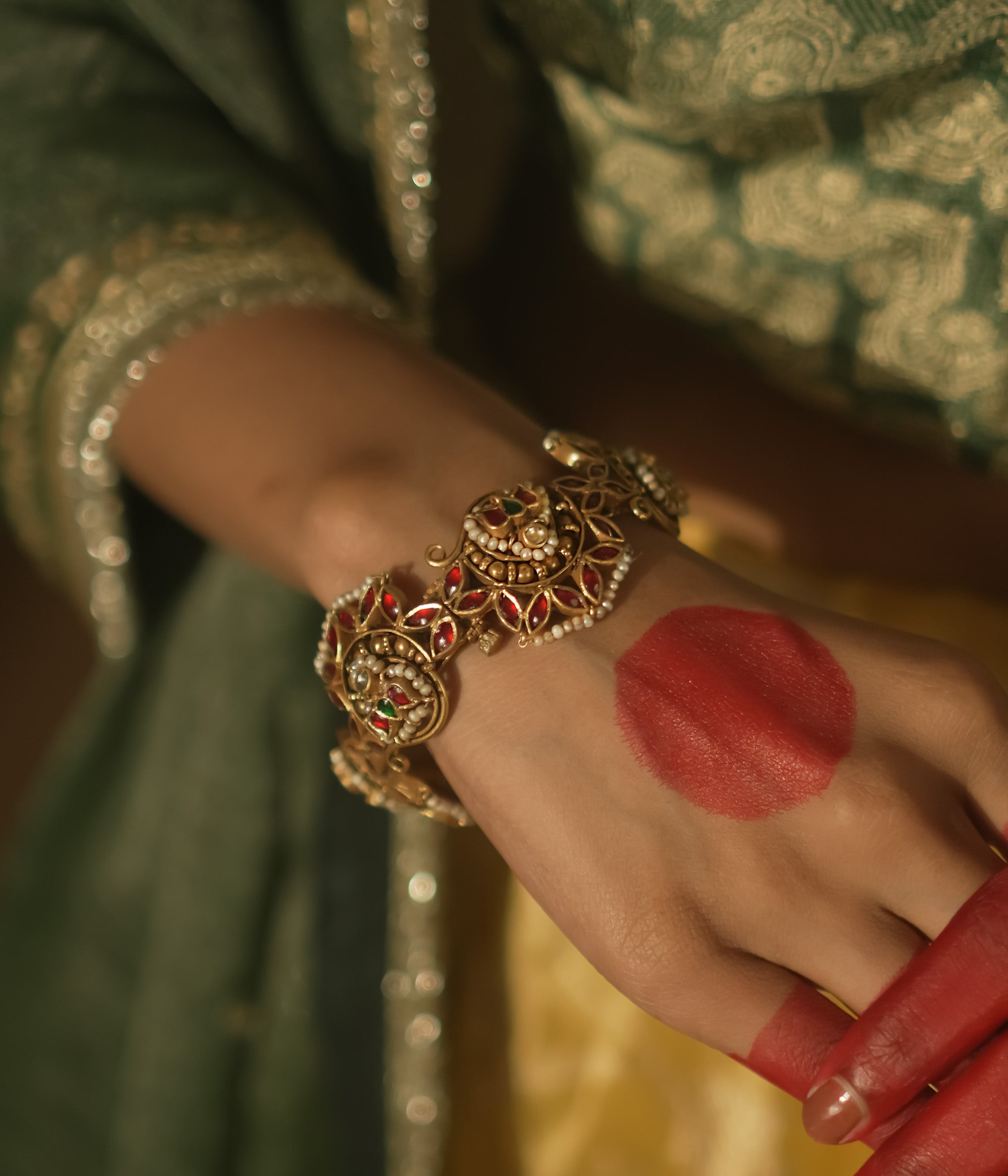 Gold-plated silver bangle with filigree, red Kundan gems, and pearls.