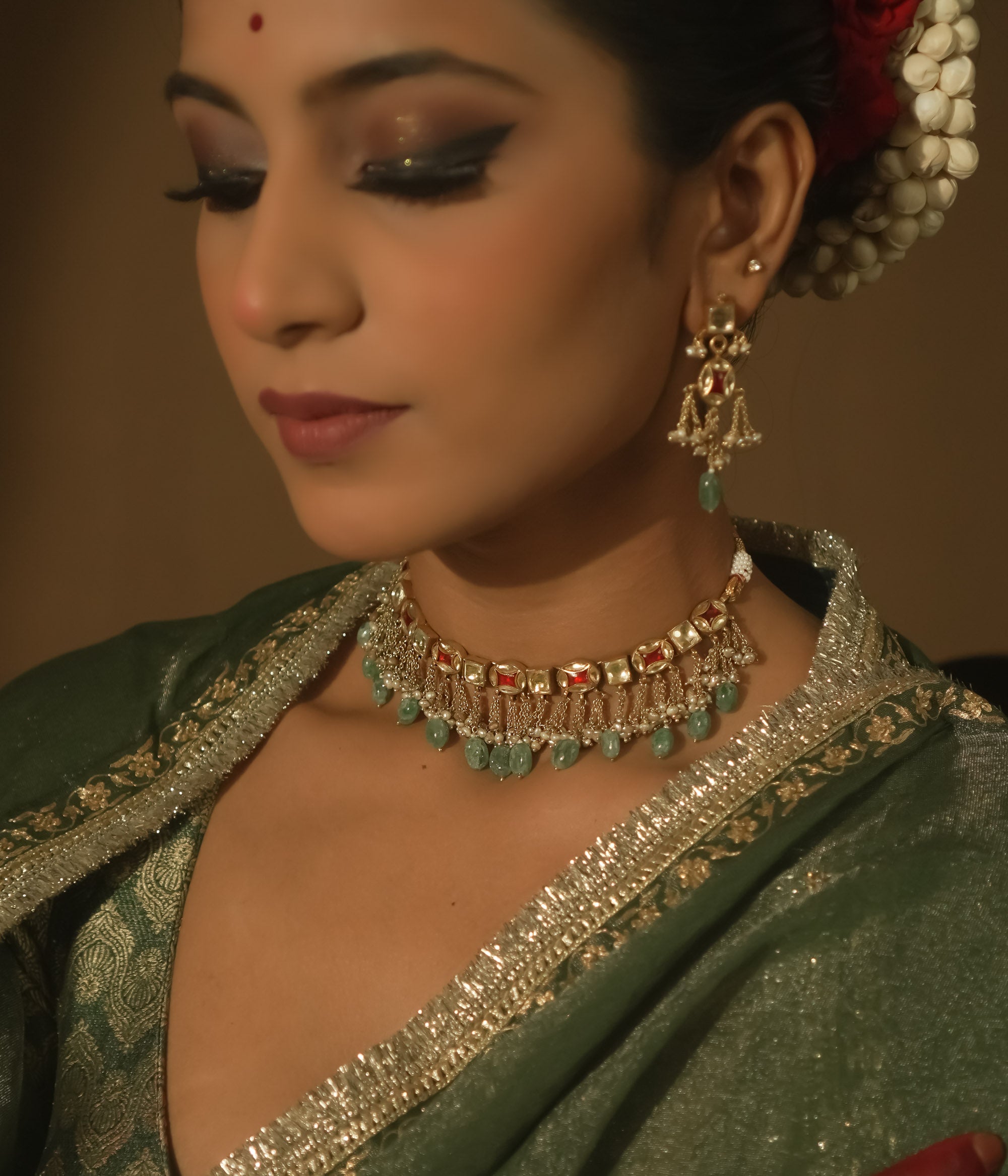 Gold necklace with tassels, clear stones, and teardrop emeralds.