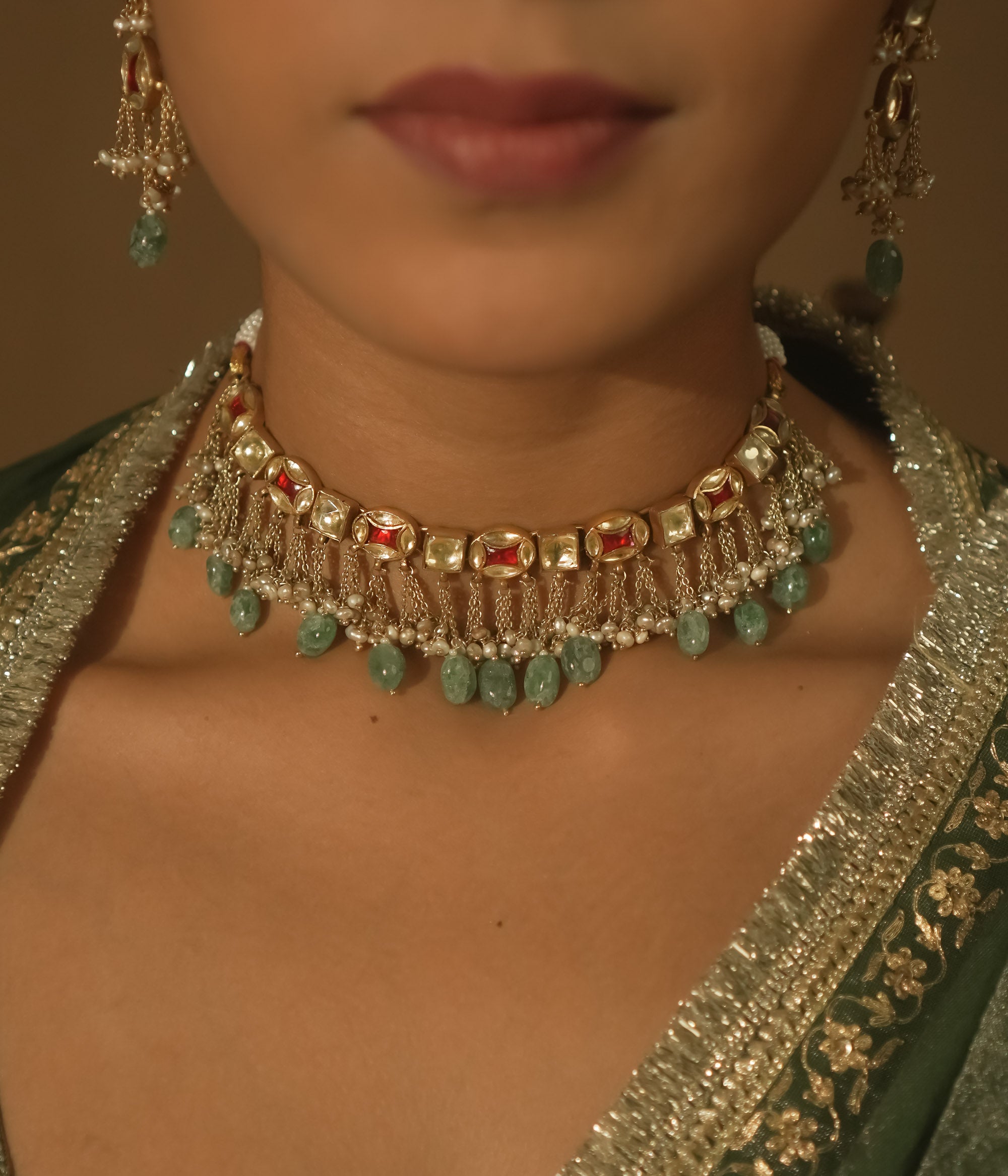 Gold necklace with tassels, clear stones, and teardrop emeralds.