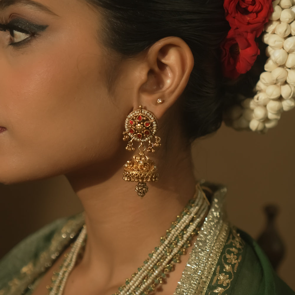 Gold earrings with intricate swirls and a central red Kundan stone.