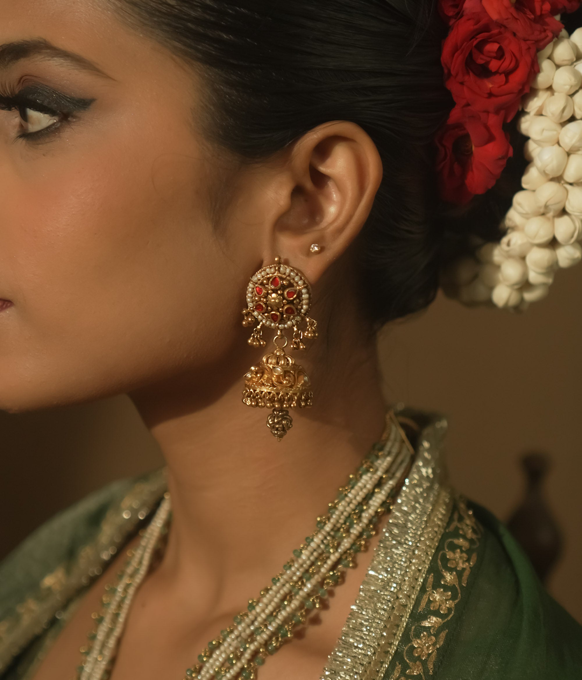 Gold earrings with intricate swirls and a central red Kundan stone.