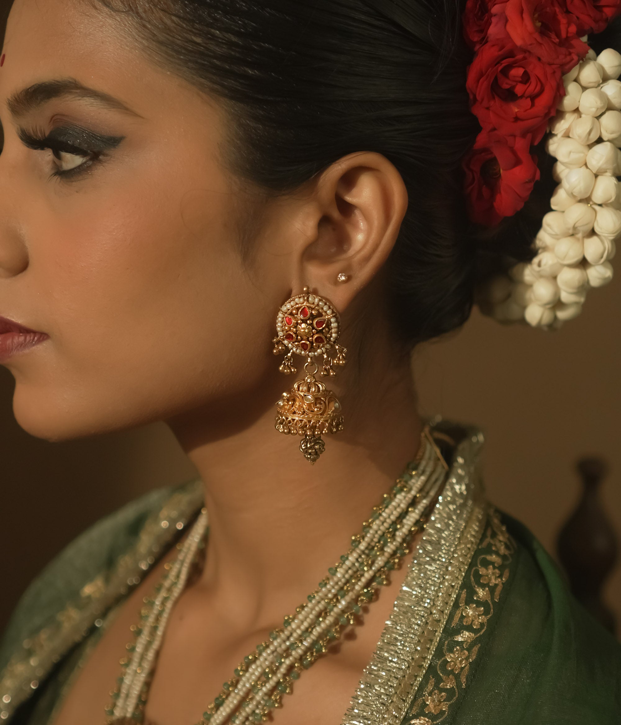 Gold earrings with intricate swirls and a central red Kundan stone.
