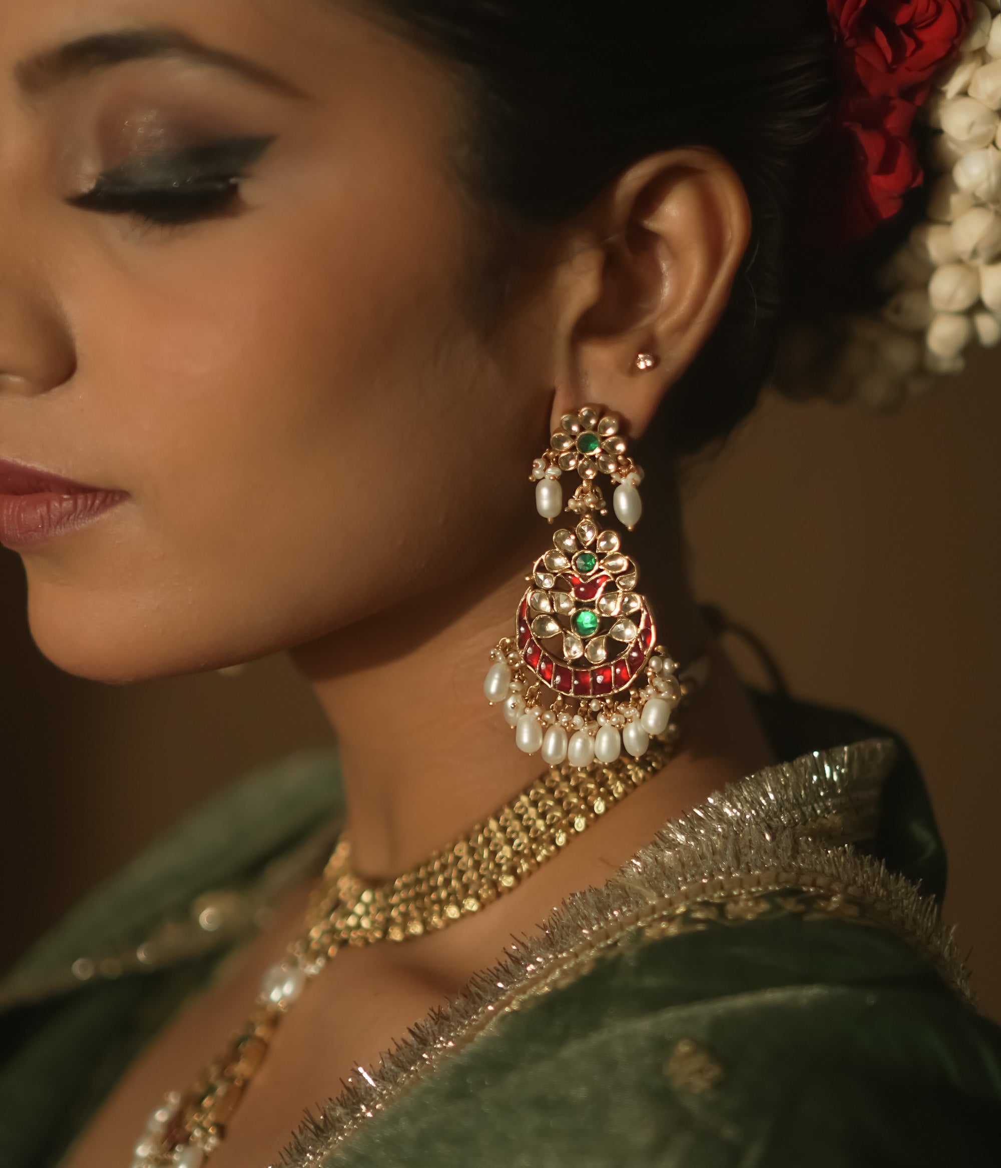 Gold teardrop earrings with red and green Kundan gems and dangling pearls.