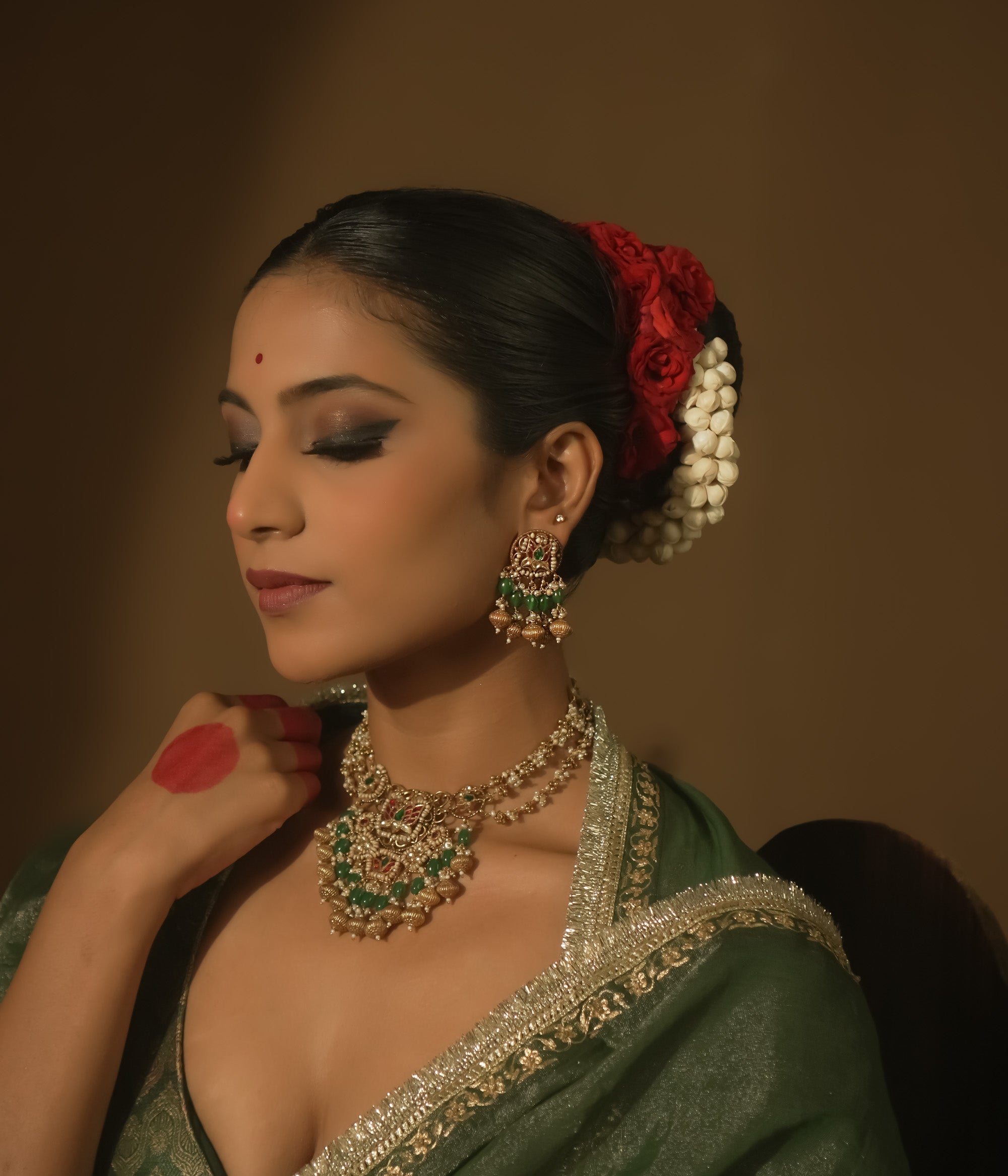 Gold jhumka earrings with green and crimson Kundan stones and pearls.