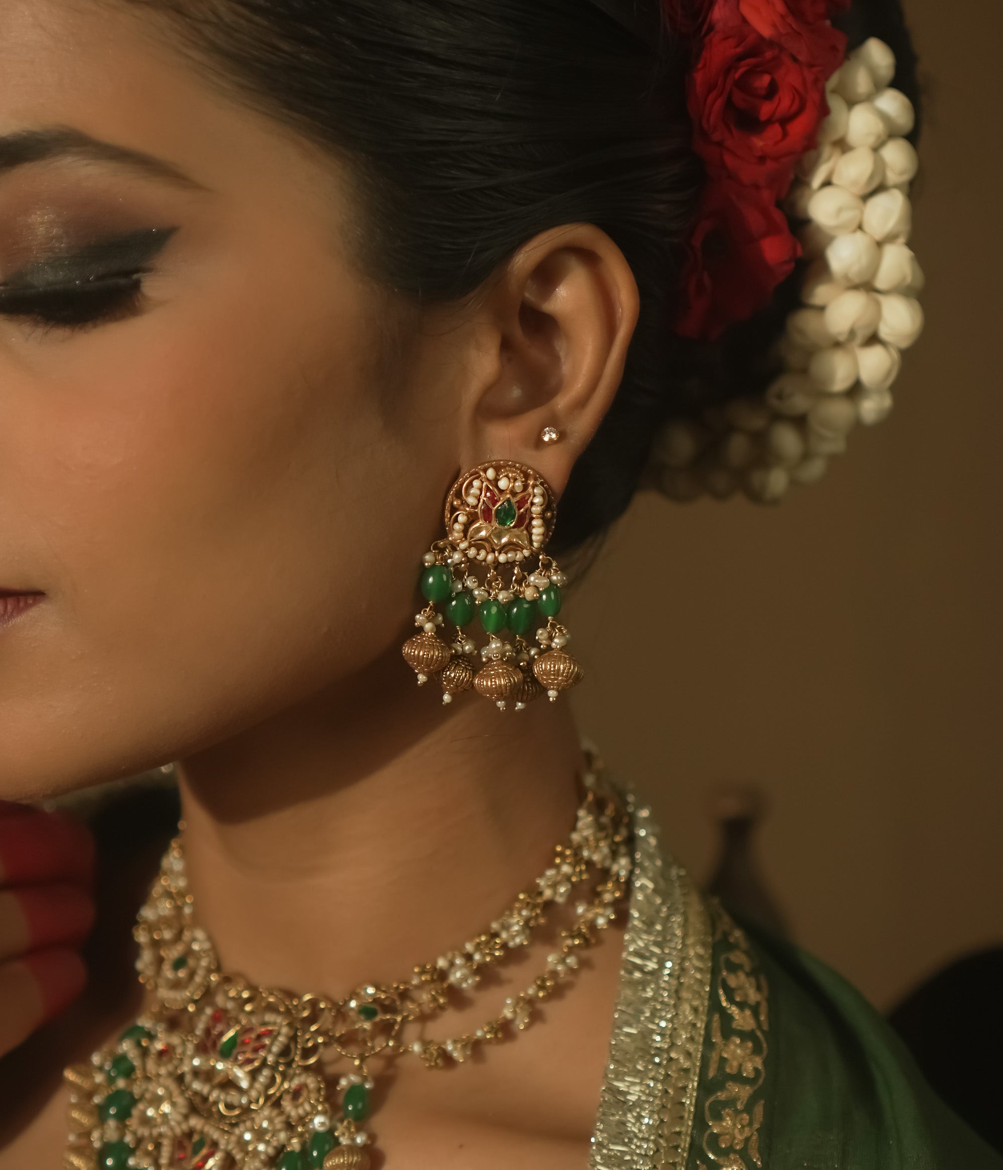 Gold jhumka earrings with green and crimson Kundan stones and pearls.