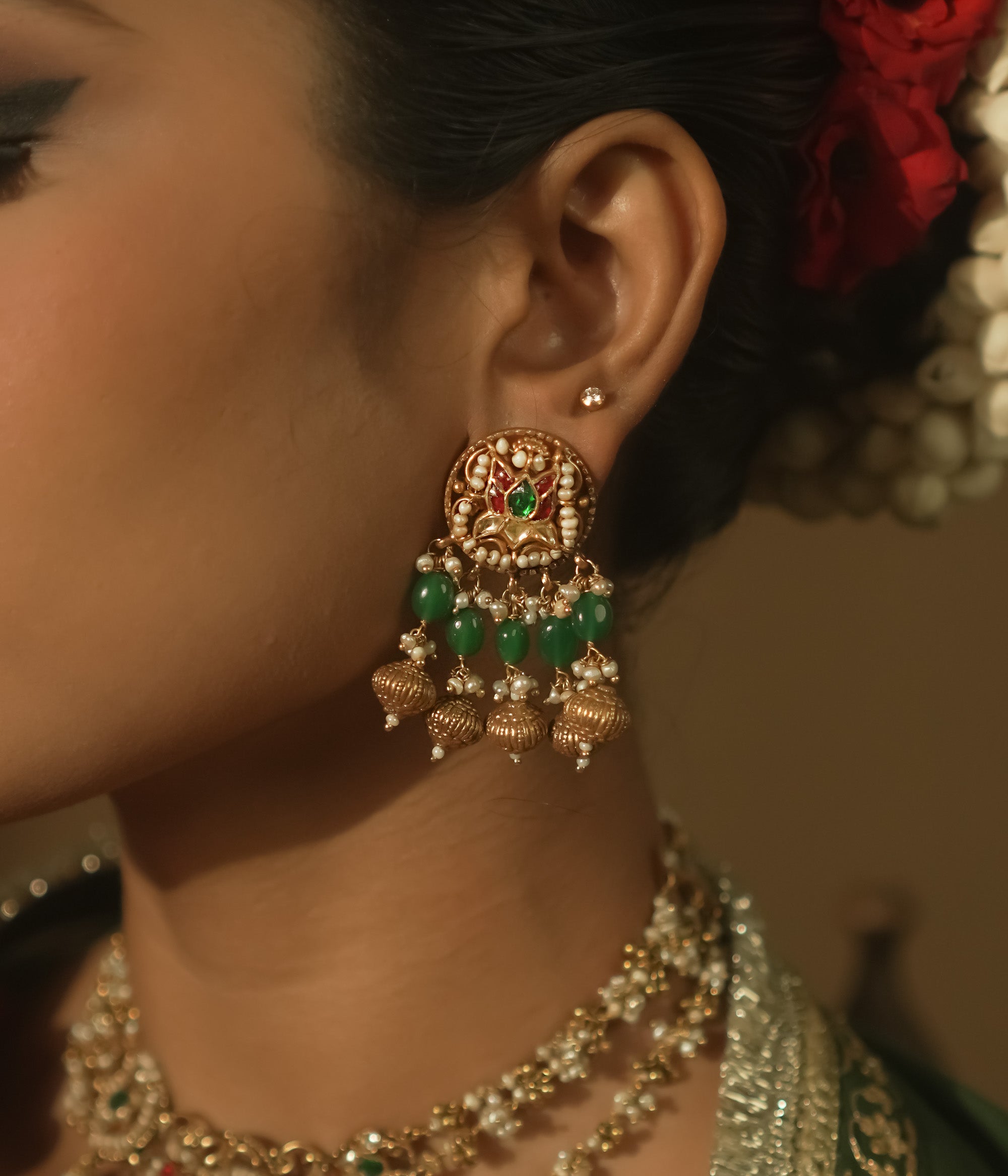 Gold jhumka earrings with green and crimson Kundan stones and pearls.
