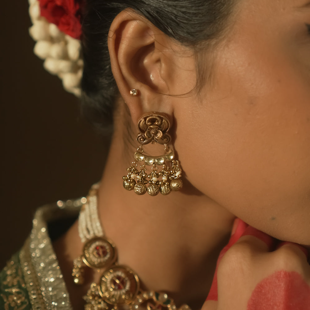 Gold chaandbali earrings with intricate swirls, red Kundan stones, and tiny bells.