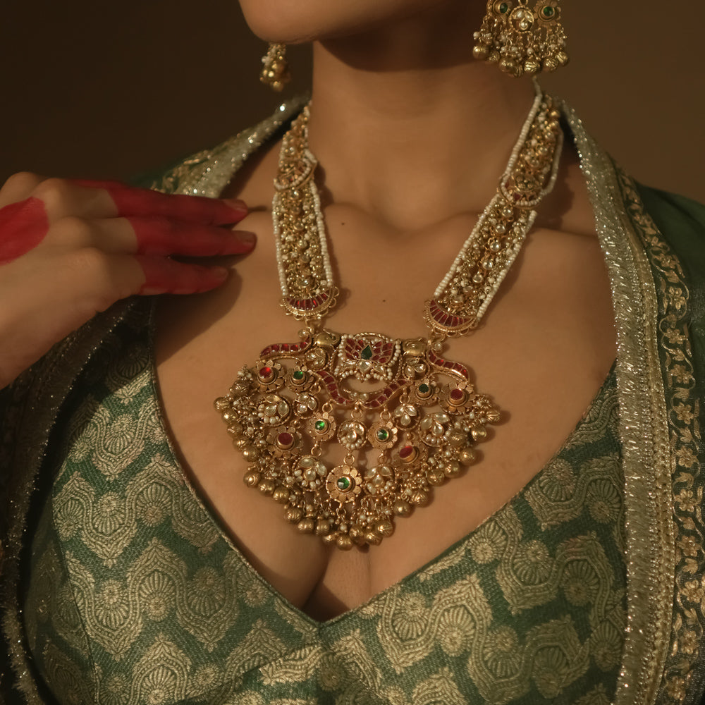 Gold-plated necklace with red and green Kundan stones, seed pearls, and dangling bells.
