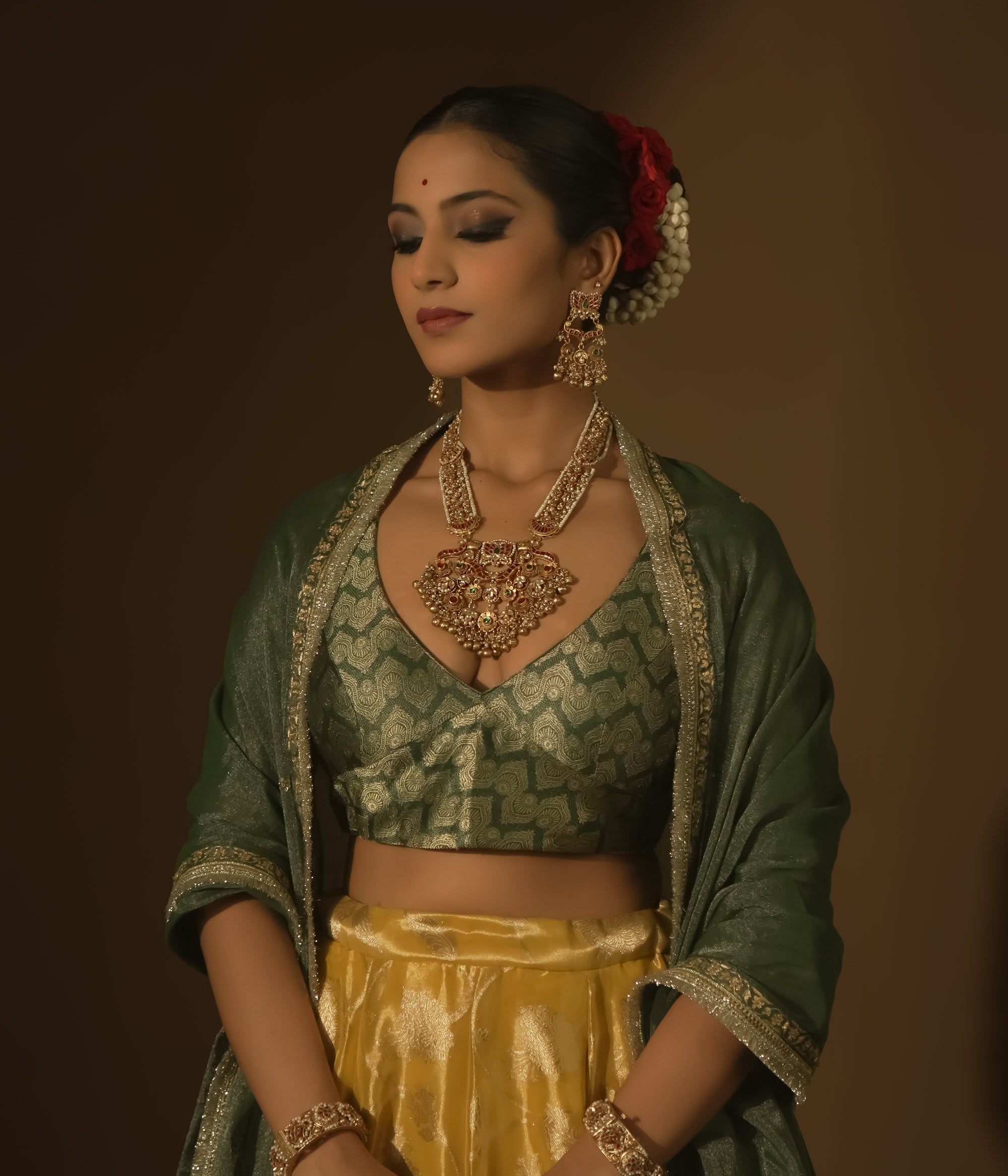 Gold-plated necklace with red and green Kundan stones, seed pearls, and dangling bells.
