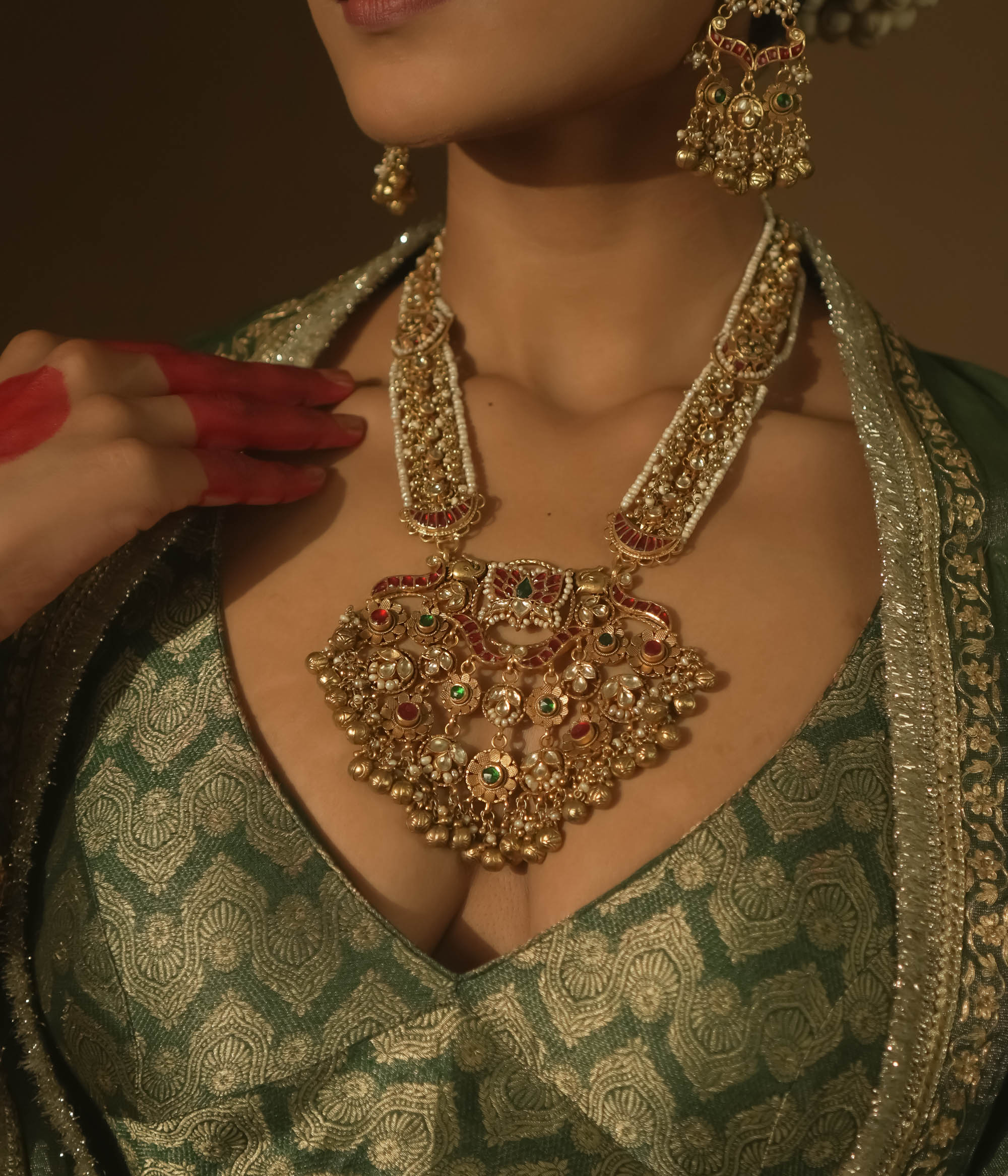 Gold-plated necklace with red and green Kundan stones, seed pearls, and dangling bells.