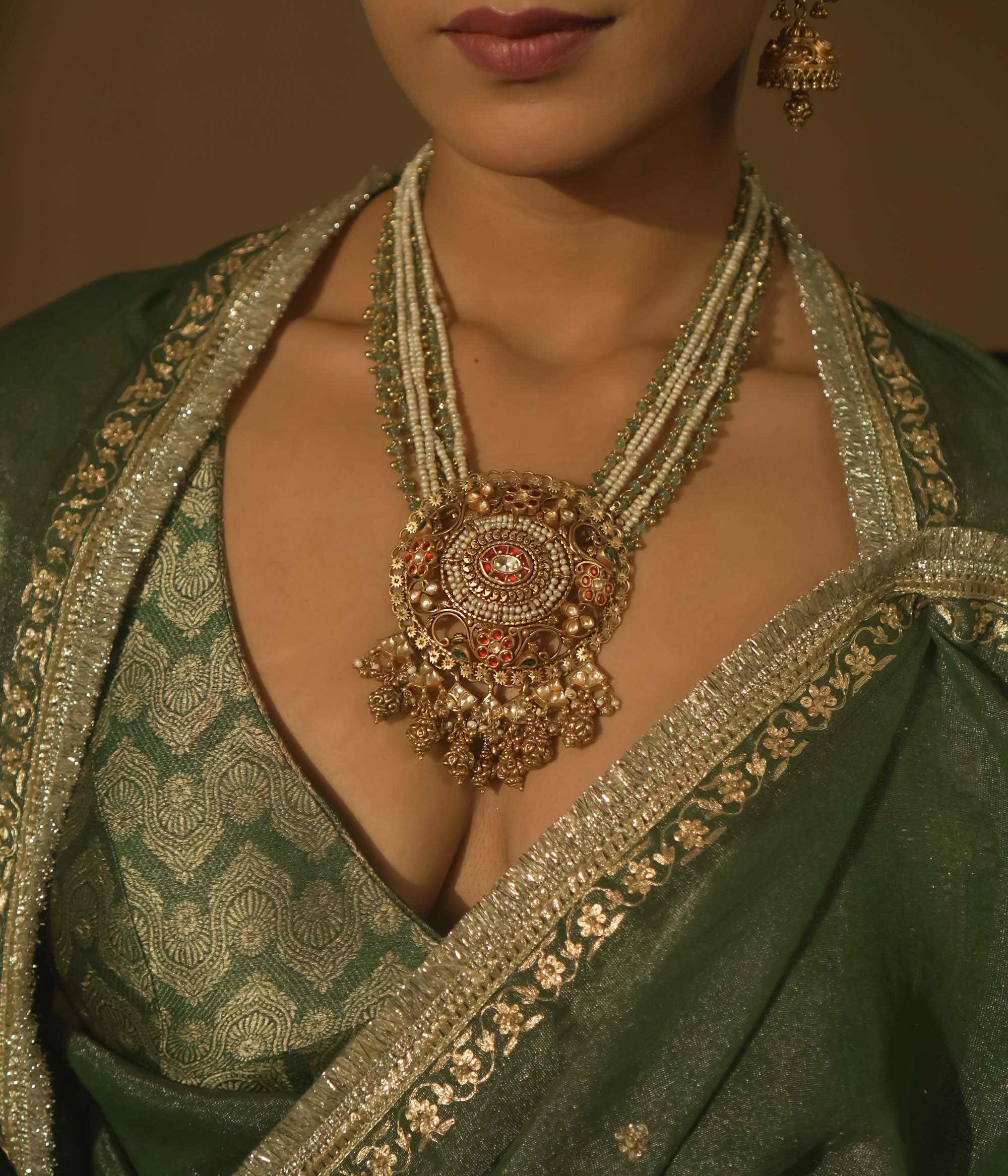 Necklace with pearls, green beads, and a central pendant with red Kundan stones.