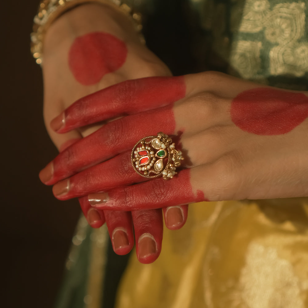 Gold ring with an intricate design, a central green Kundan stone, and pearls.