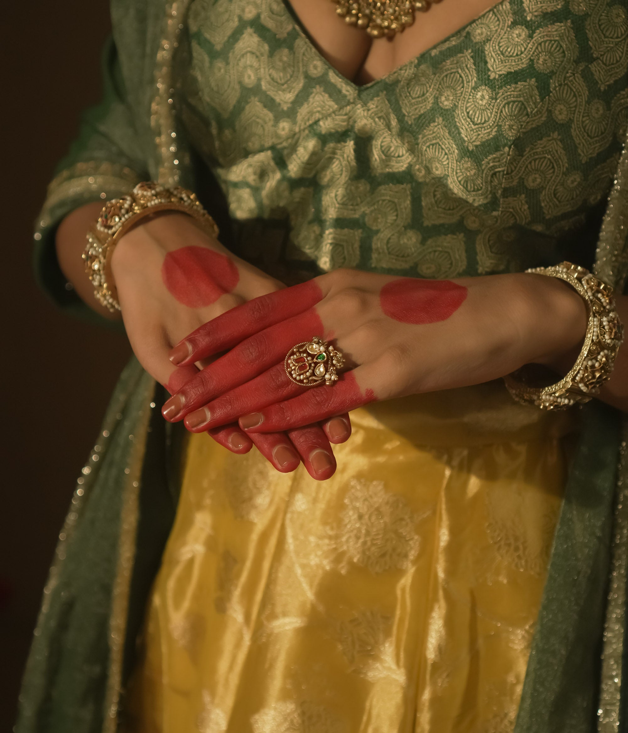Gold ring with an intricate design, a central green Kundan stone, and pearls.