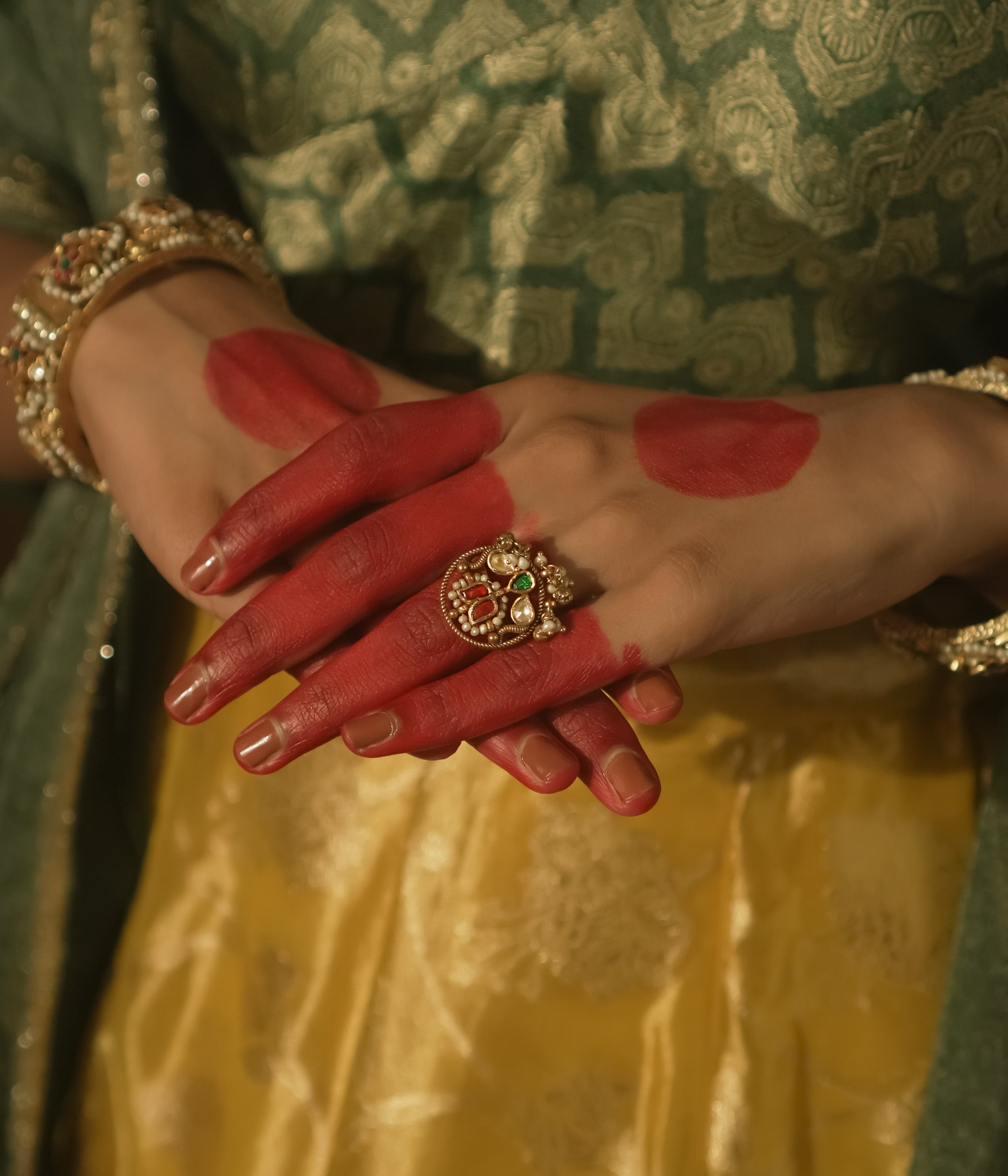 Gold ring with an intricate design, a central green Kundan stone, and pearls.