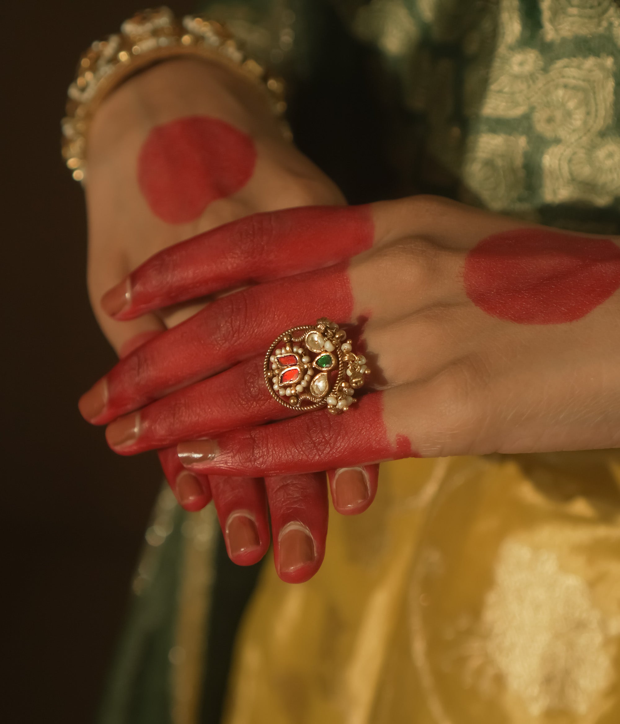 Gold ring with an intricate design, a central green Kundan stone, and pearls.