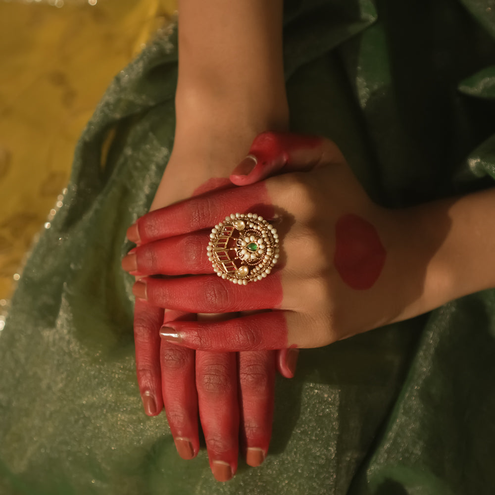 Gold ring with a swirl design, pearls, and red and green Kundan stones.