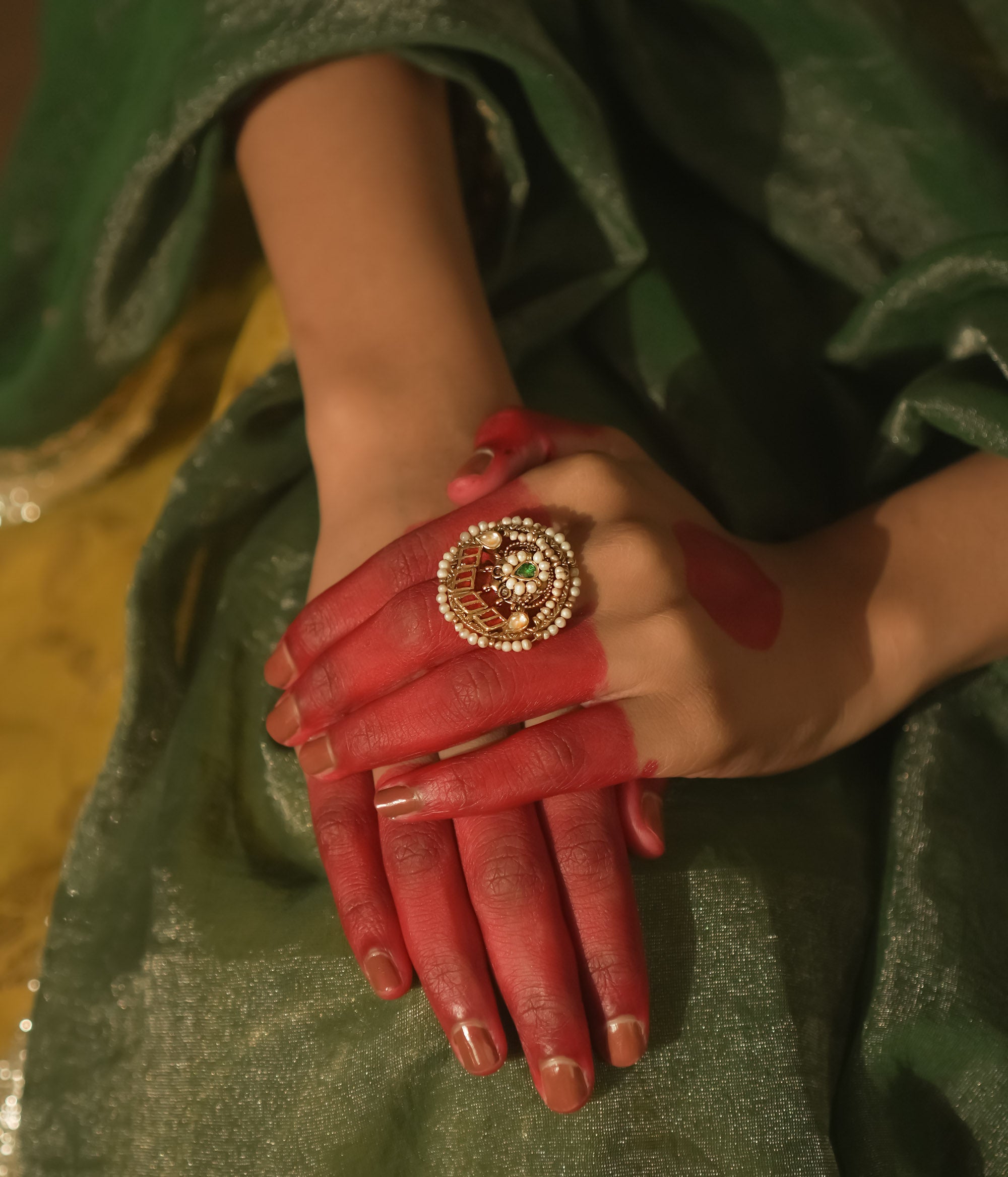 Gold ring with a swirl design, pearls, and red and green Kundan stones.