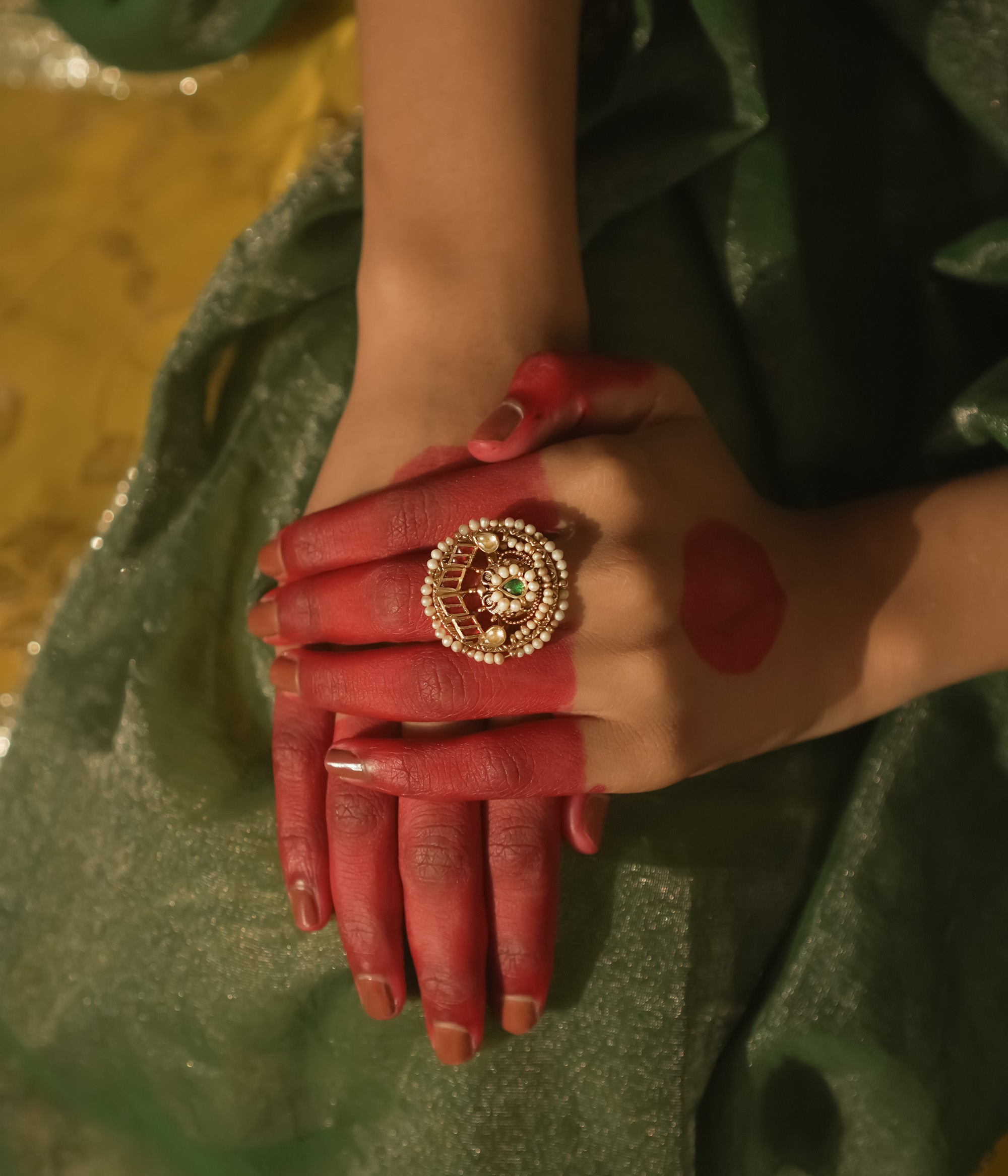 Gold ring with a swirl design, pearls, and red and green Kundan stones.