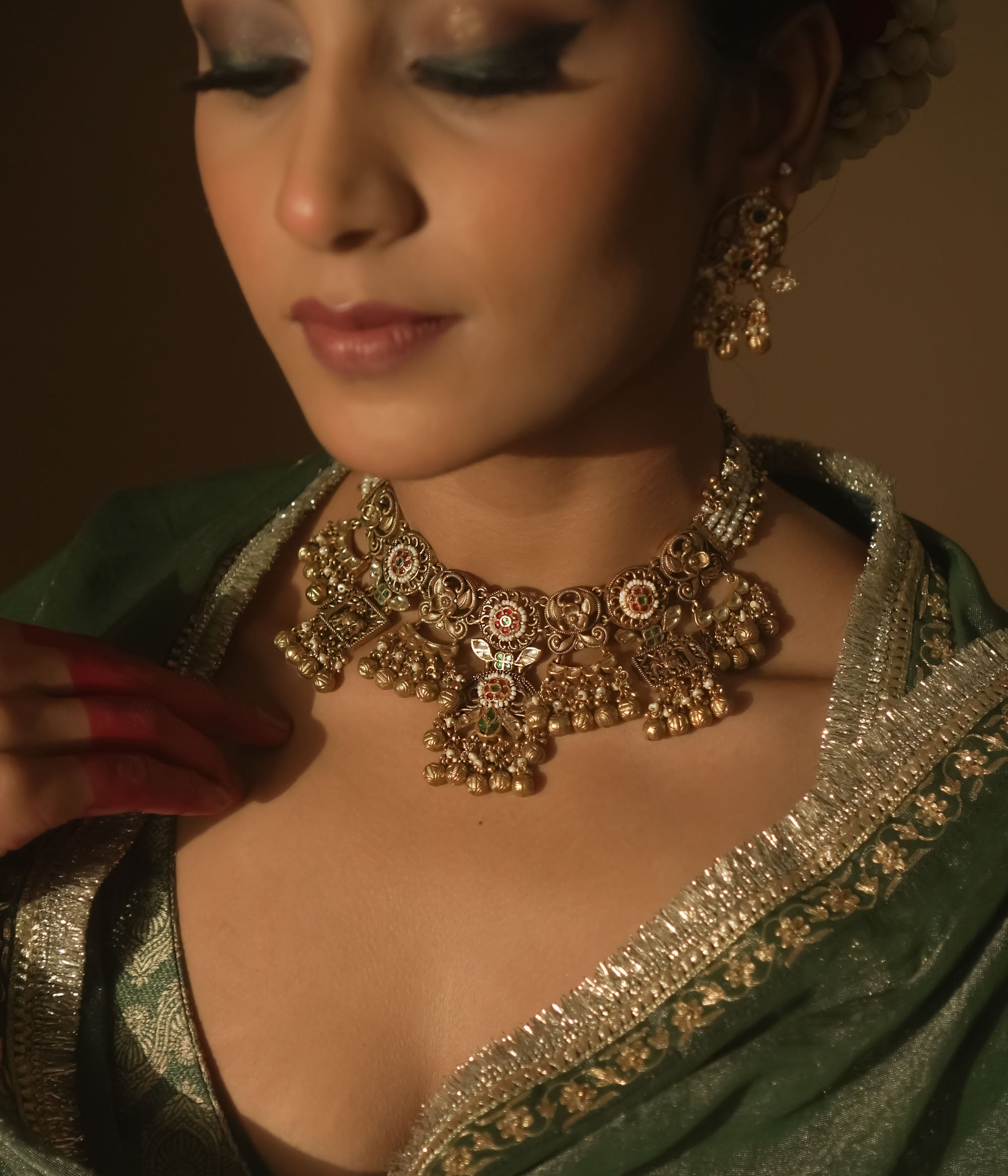 Gold-plated necklace with intricate swirls, red, green, and white gems, pearls, and bells.